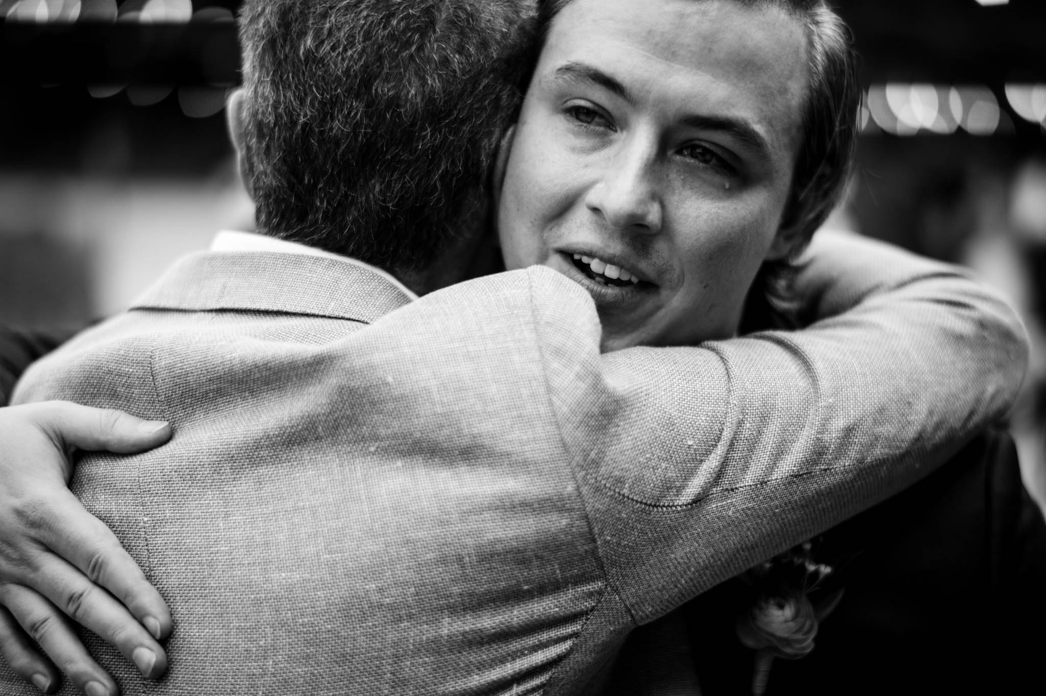 a groom cries while hugging family after his wedding ceremony