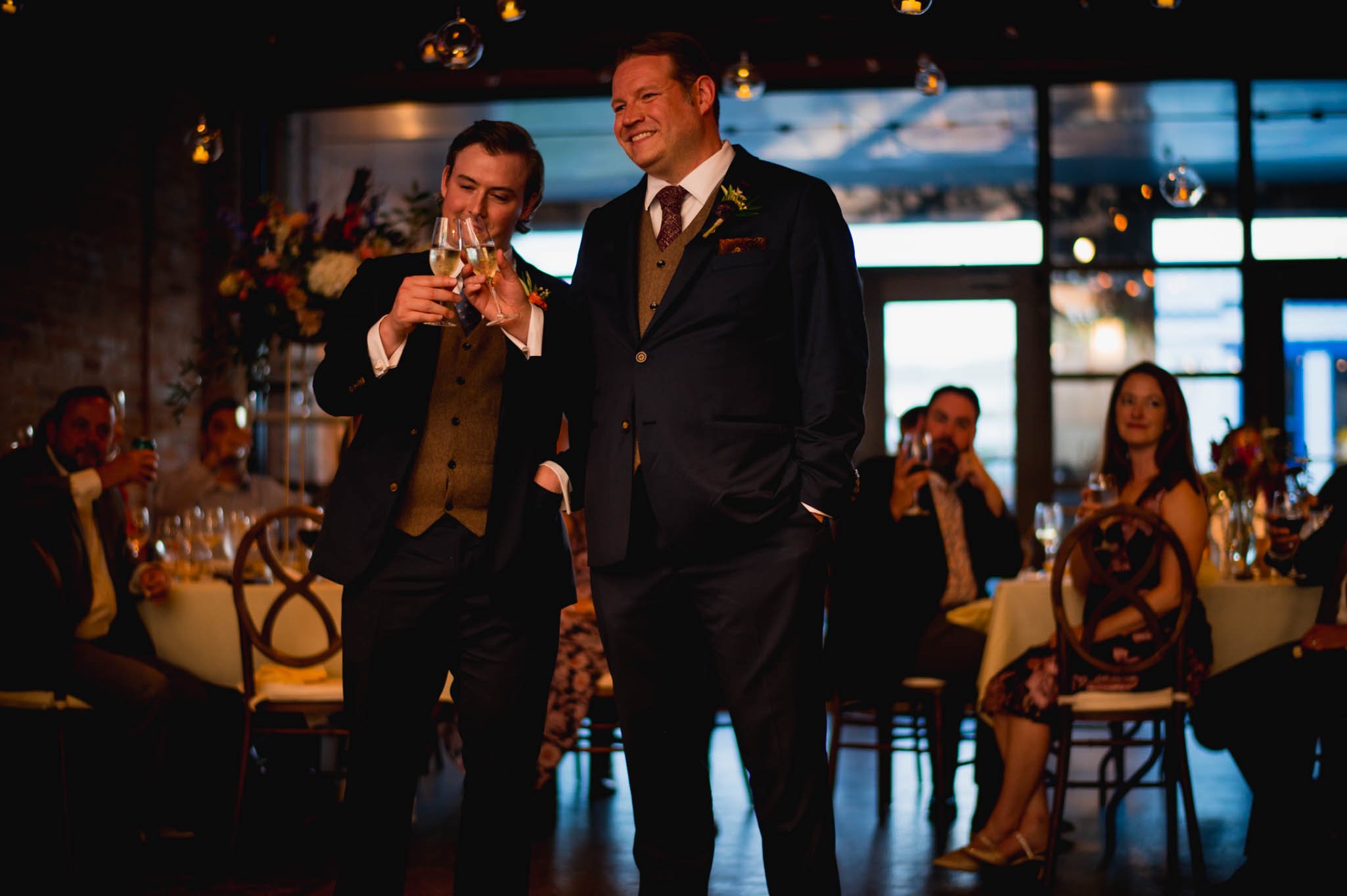 the two grooms look on during toasts