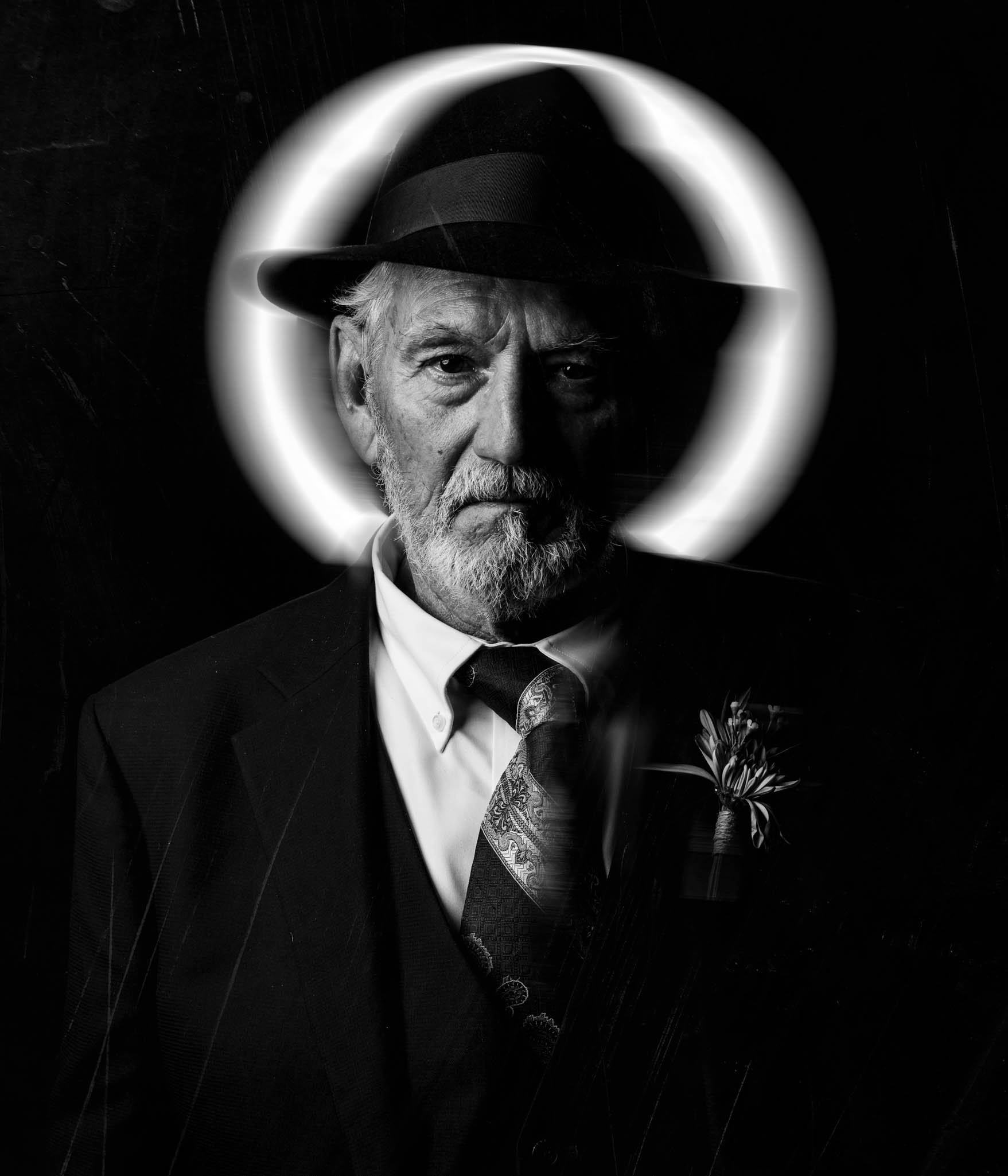 father of the groom poses with fedora and light halo behind his head