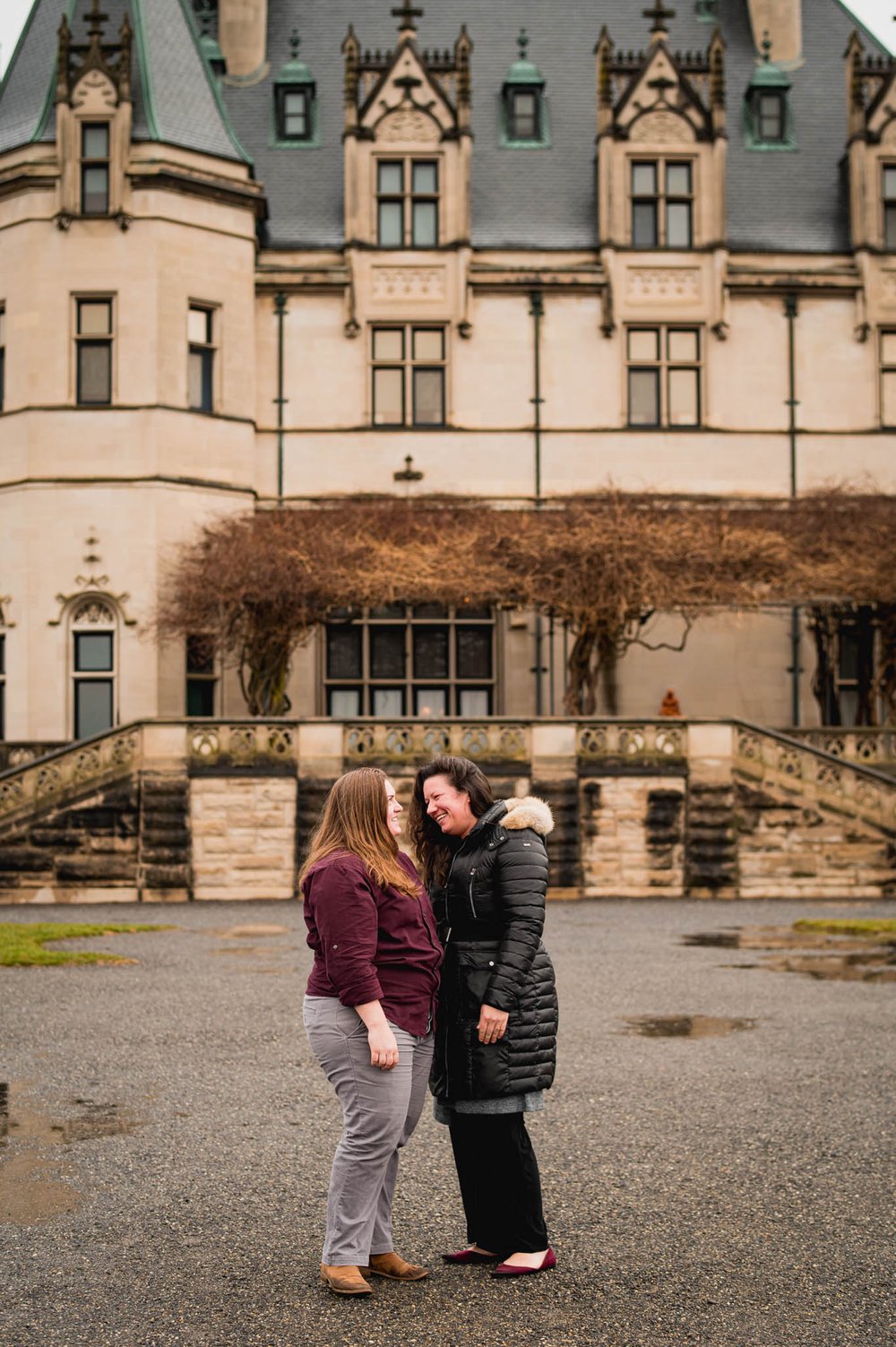 couple stands in front of the Biltmore house in the rain