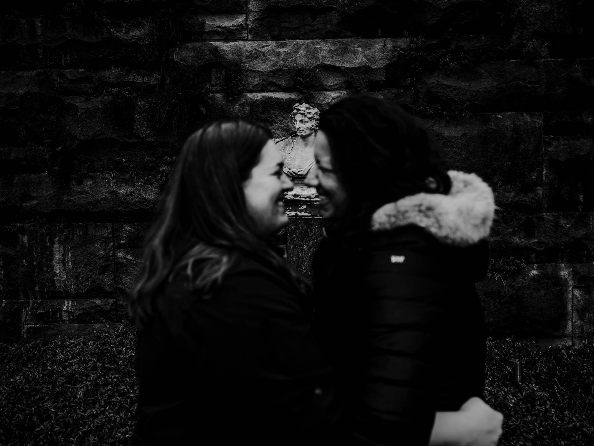 a statue in the background staring off as a couple embraces