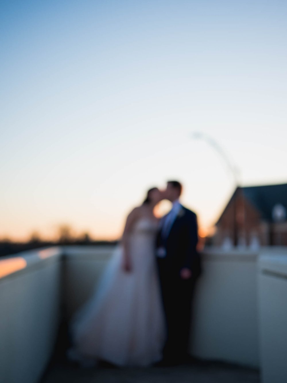 blurred photo of bride and groom kissing in the light of the sunset after their wedding