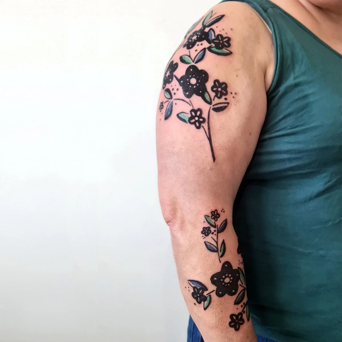 Tatouage floral sur mesure en noir et vert sur le bras réalisé par Camille Tardif