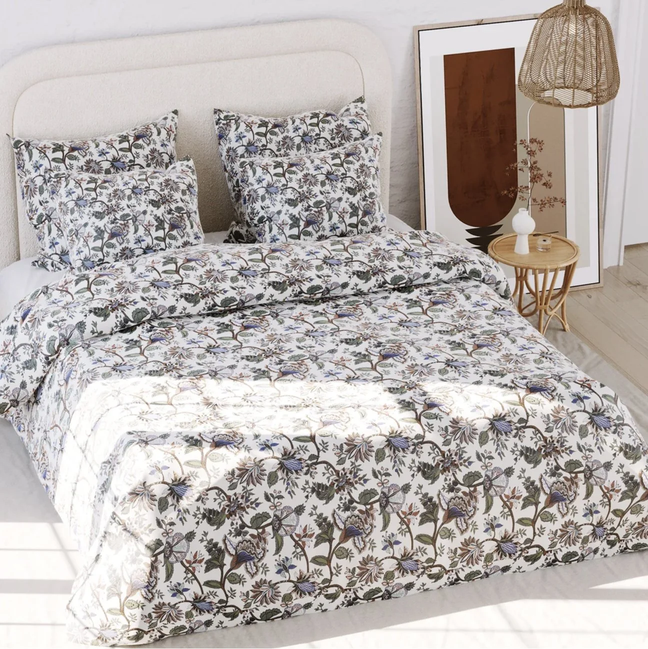 Linge de lit avec motif floral sur un lit, avec des oreillers assortis. Chambre décorée avec une œuvre d'art encadrée, une lampe en rotin et une petite table en bois.