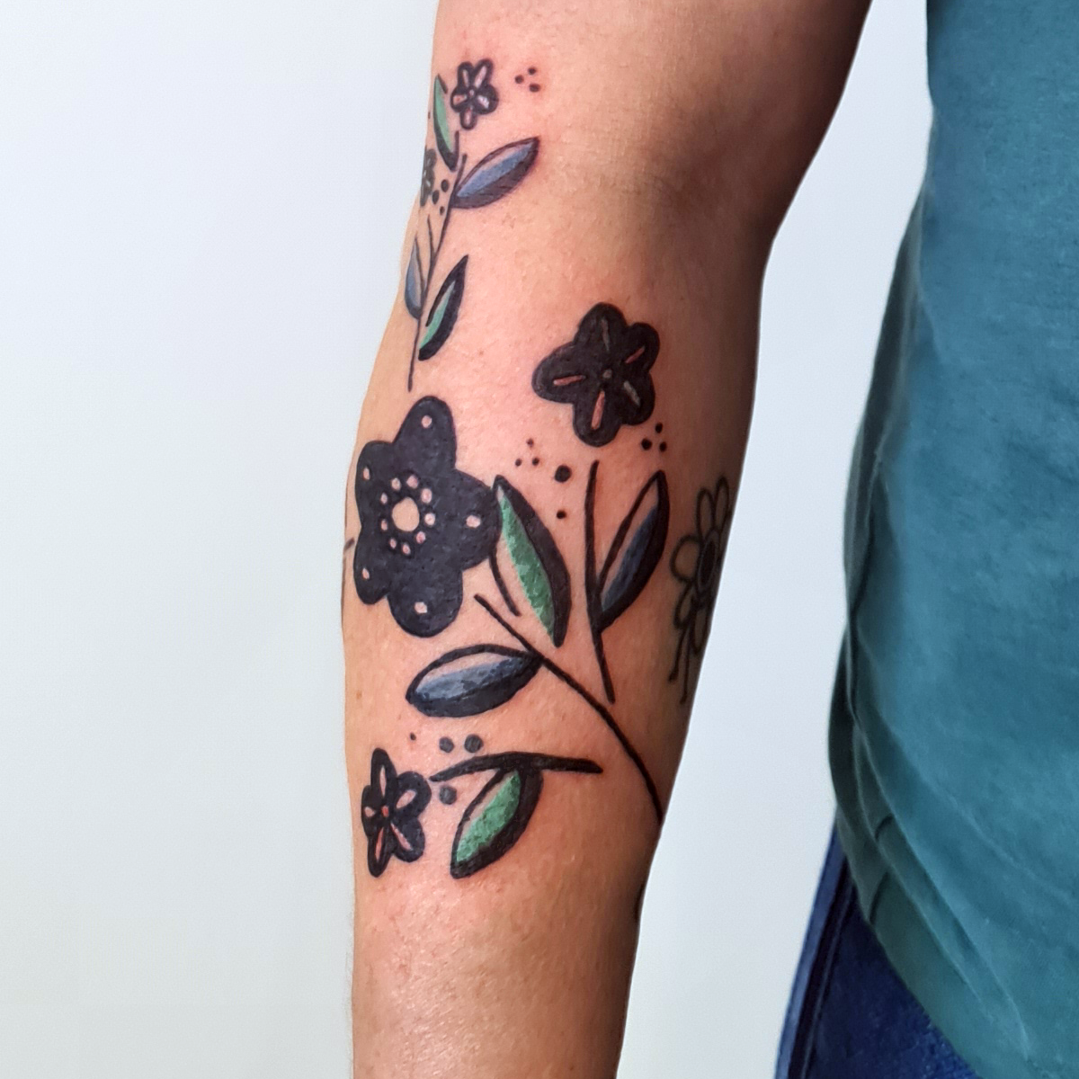 Tatouage de fleurs stylisées avec des feuilles vertes sur le bras d'une personne.