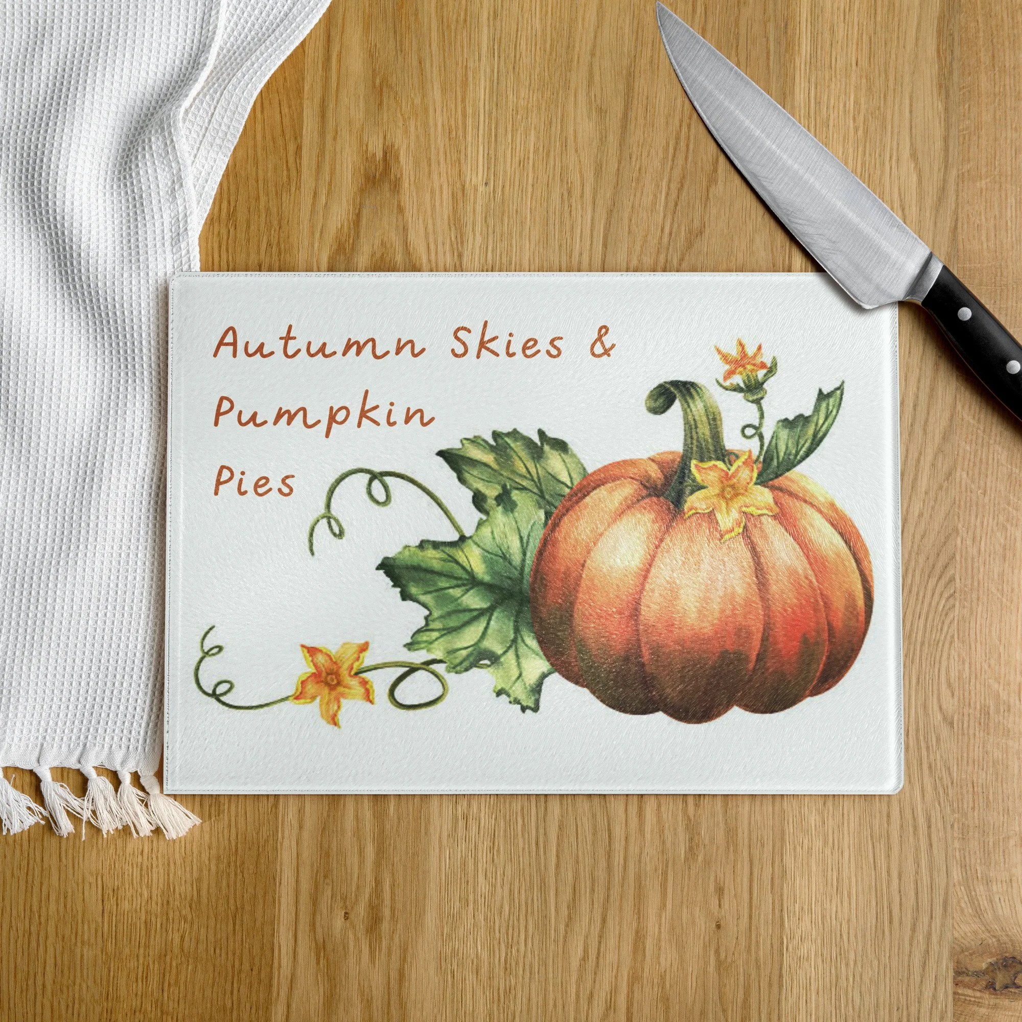 Tempered glass cutting board featuring a pumpkin with twisting vines, tendrils, leaves and yellow squash blossoms. Text reads "Autumn Skies and Pumpkin Pies."