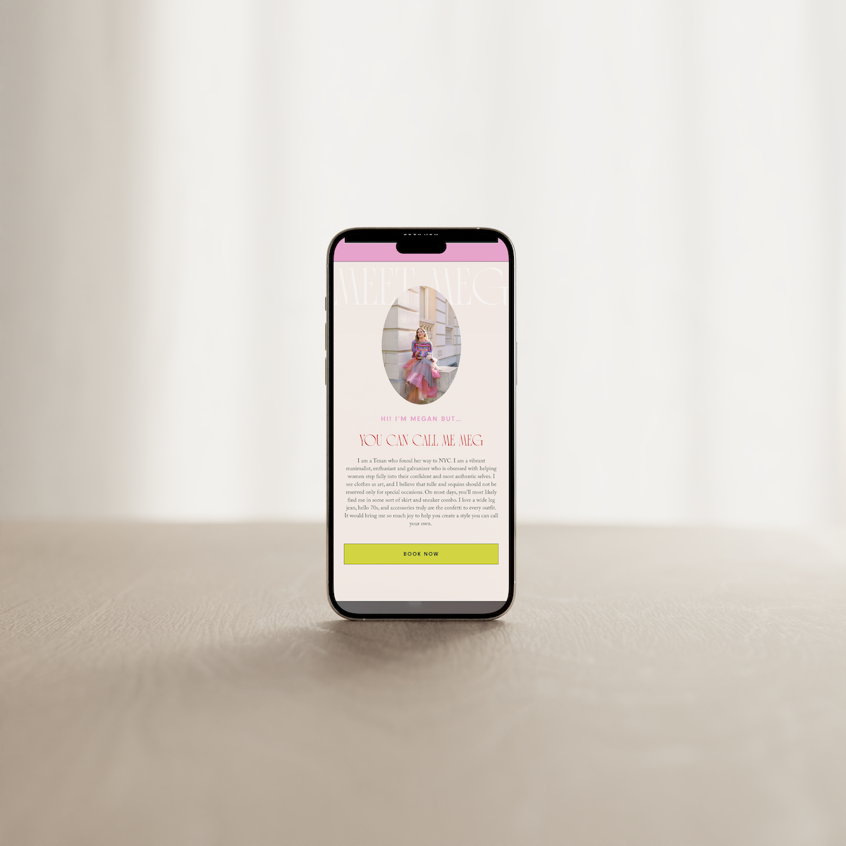 Smartphone displaying a personal website or profile page of Megan, a fashion enthusiast, with a photo of her sitting outside, a greeting message, and a call-to-action button labeled 'BOOK NOW' on a neutral background.