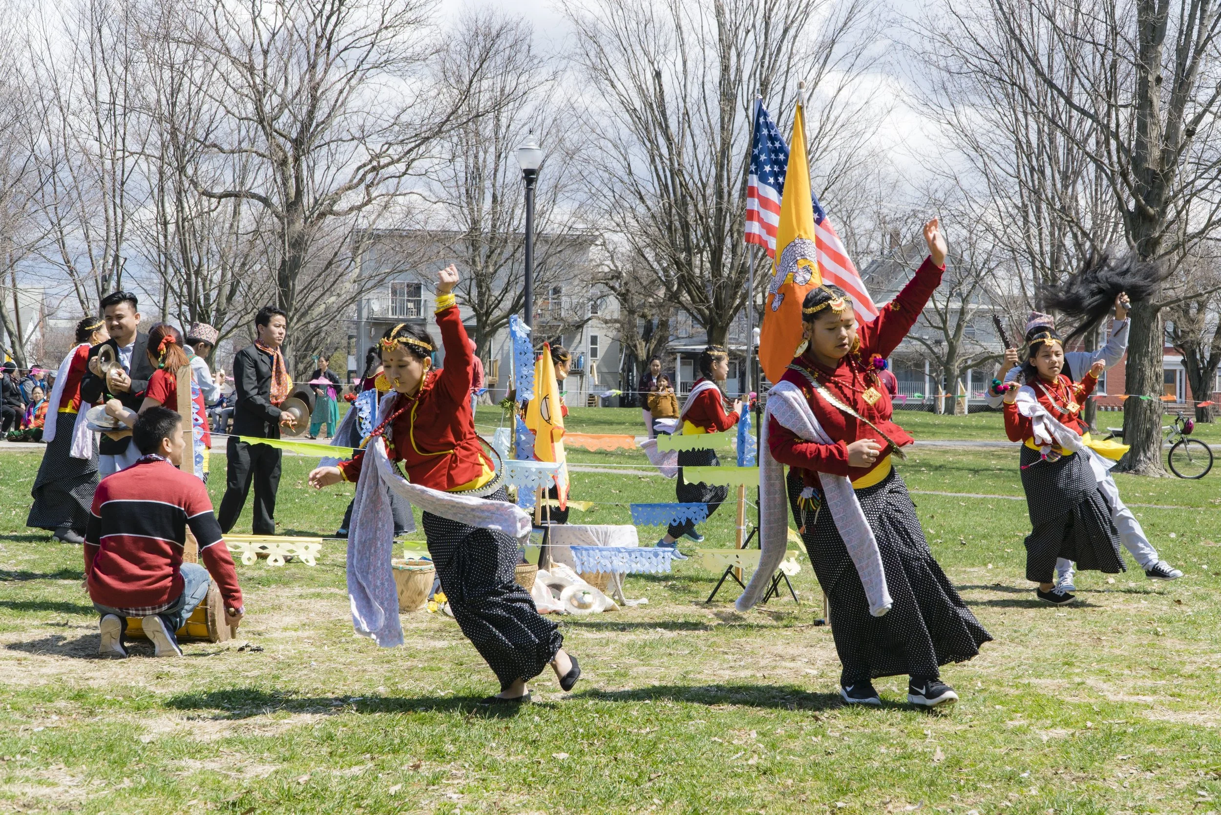 Several girls in Nepali traditional dress dance around flags, while musicians play symbols. 