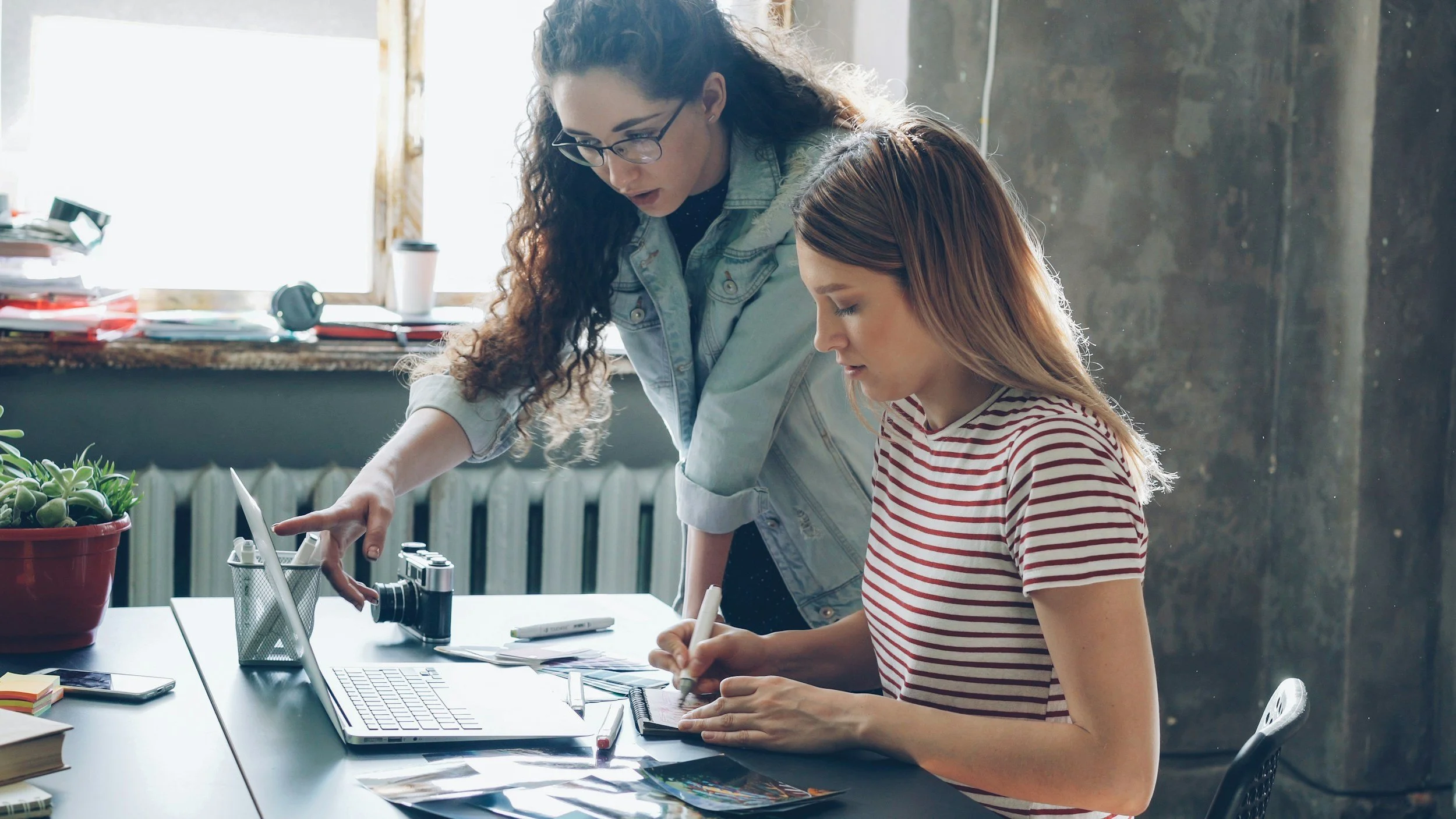 Two women working together at a desk, illustrating workplace communication, people-pleasing, and setting healthy boundaries.