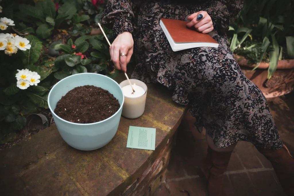 Lighting the Luminous Meadow ritual candle with a match beside a planting bowl of soil, marking the start of an Ostara Spring Equinox ritual