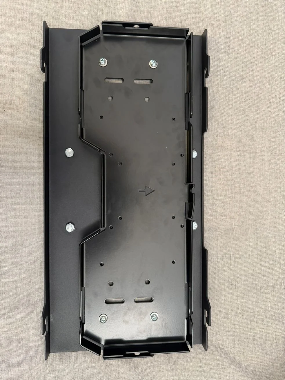 Empty black metal mounting bracket with screws, on a beige fabric background.