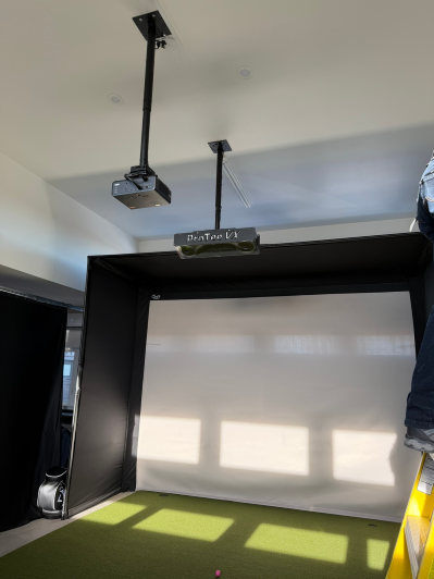 Indoor golf simulator setup with a projection screen and ceiling-mounted projector