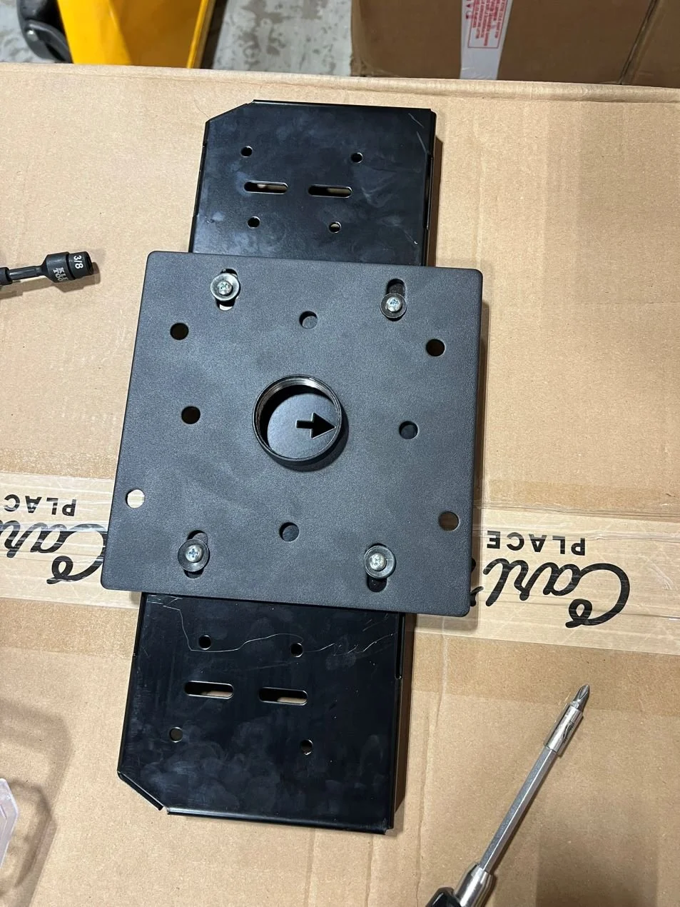 Two black metal mounting brackets and a screwdriver resting on a cardboard box.