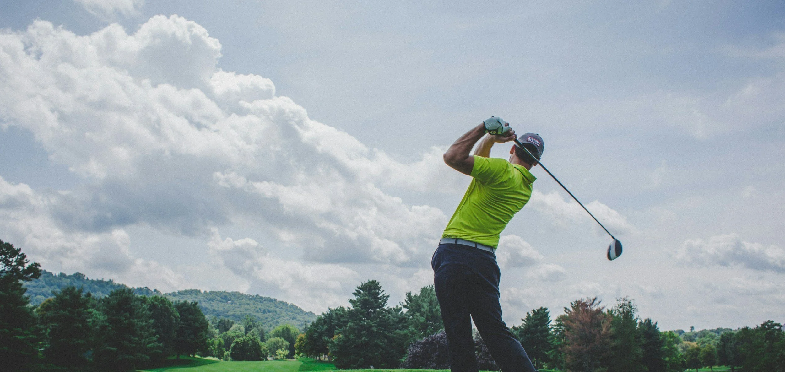 Golfer hitting a driver on an outdoor golf course under a cloudy sky, illustrating how simulator practice can complement real course play.