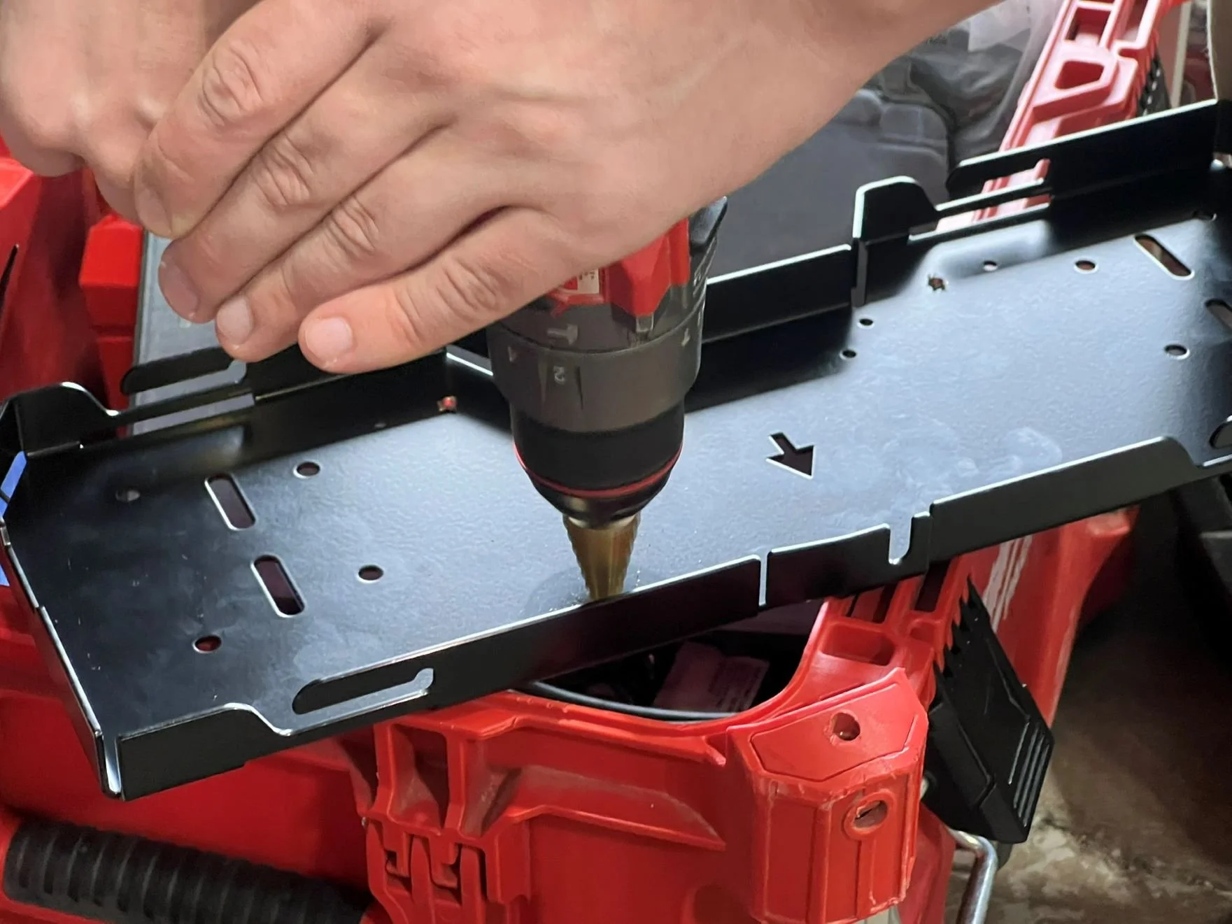 Person using a cordless drill to assemble a metal frame and a red plastic toolbox.