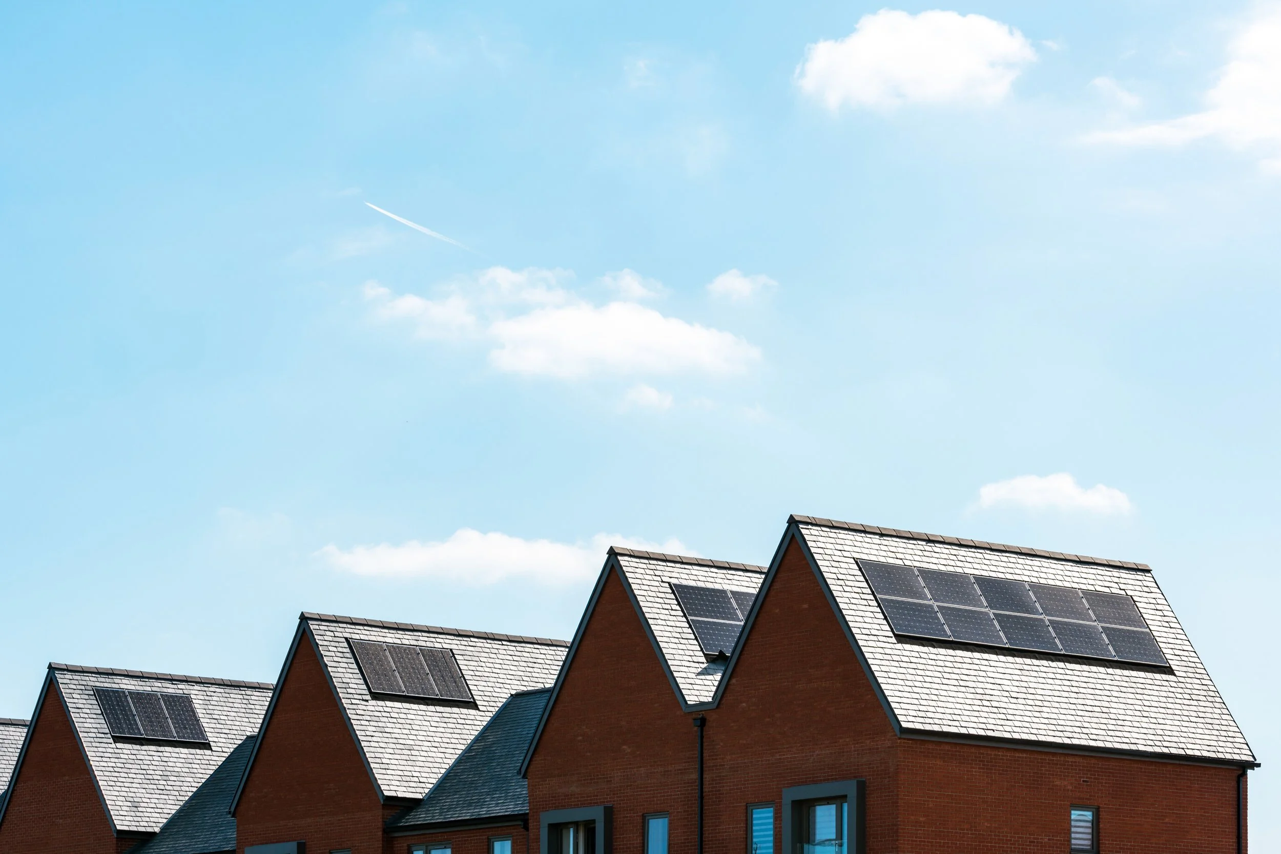 Red brick houses with solar panels on the roofs under a partly cloudy blue sky.