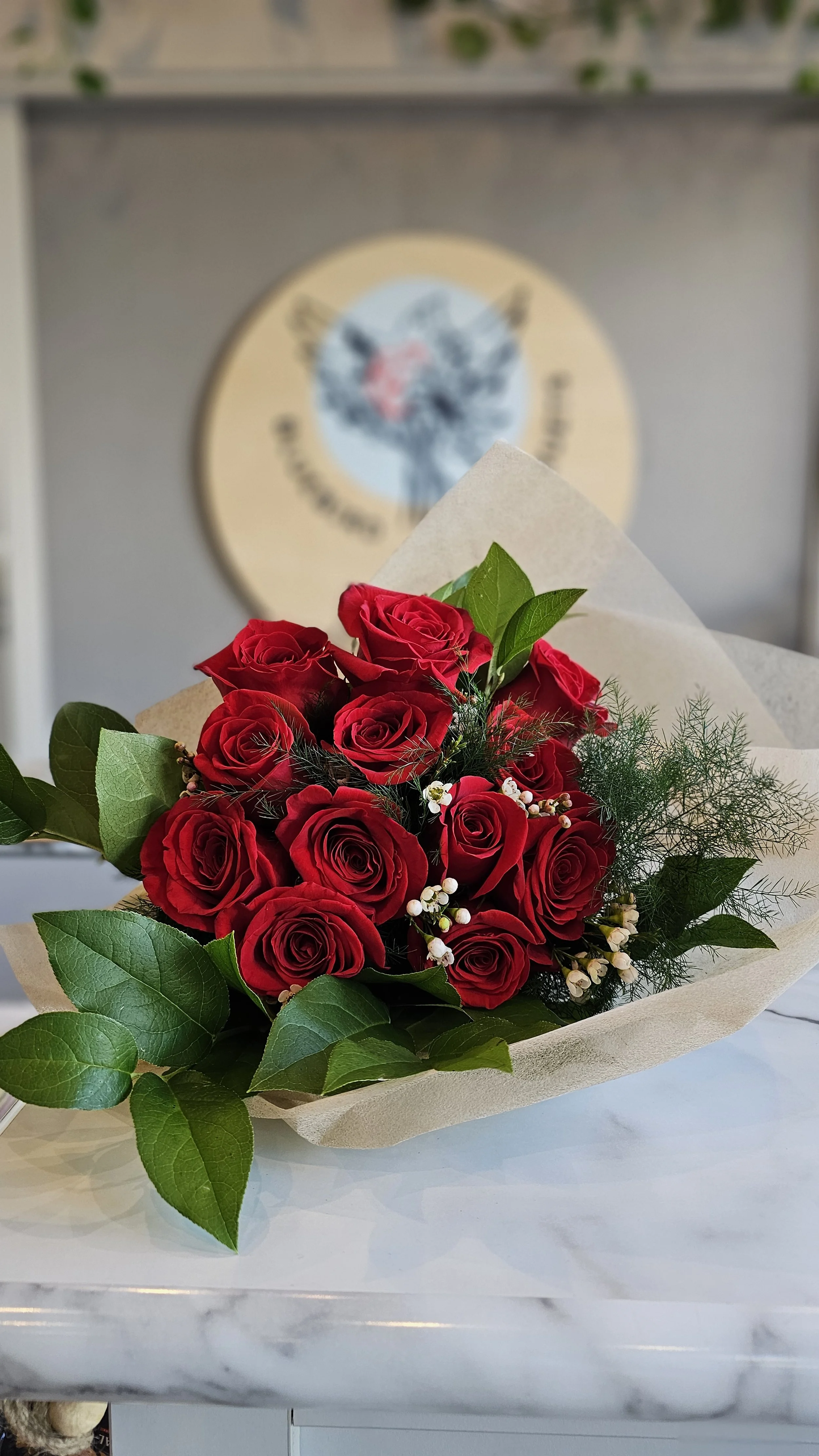 Bouquet of red roses with green leaves and small white flowers on a marble countertop.