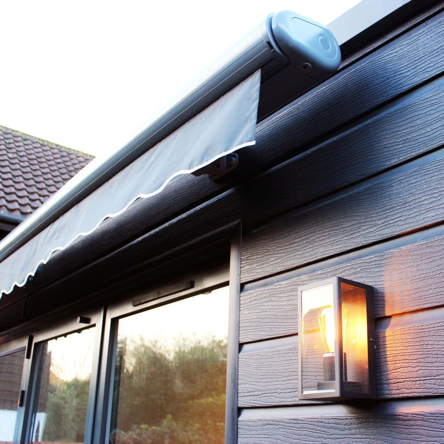 Modern house extension with black cladding around bifold doors. The design features a remote-controlled awning for solar shading and an exterior lamp for lighting the patio area.

#houseextension #awning #architecture