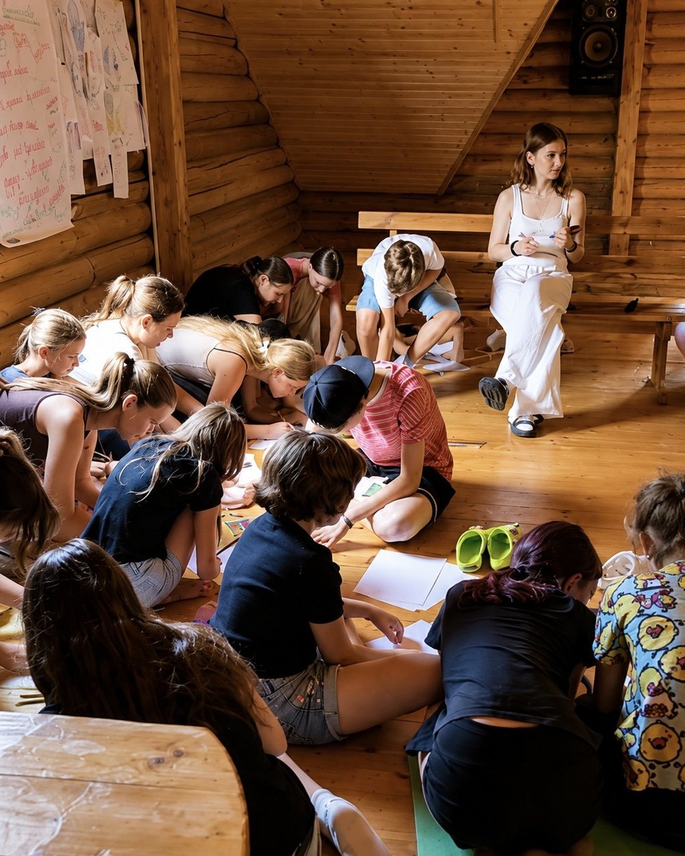 Children sit on the floor of an attic room listening to a young woman leading a group session.