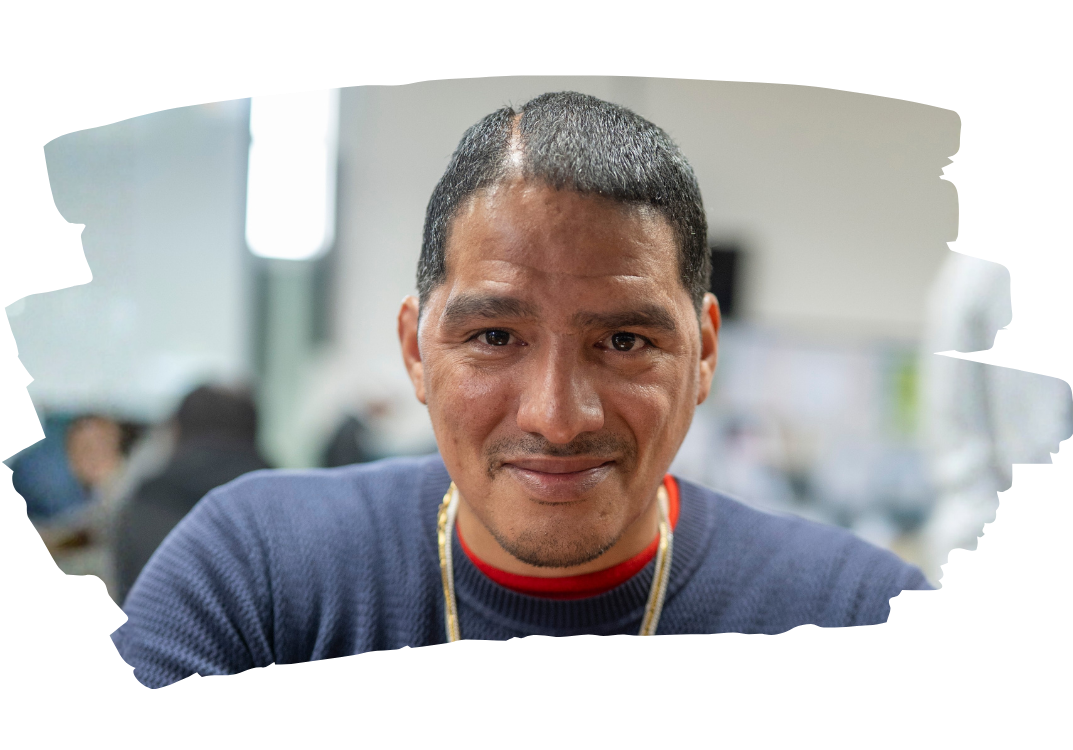 Click to read Angel's story of recovery and hope. Photo shows a puerto rican man smiling proudly in the dining room of Philly House.