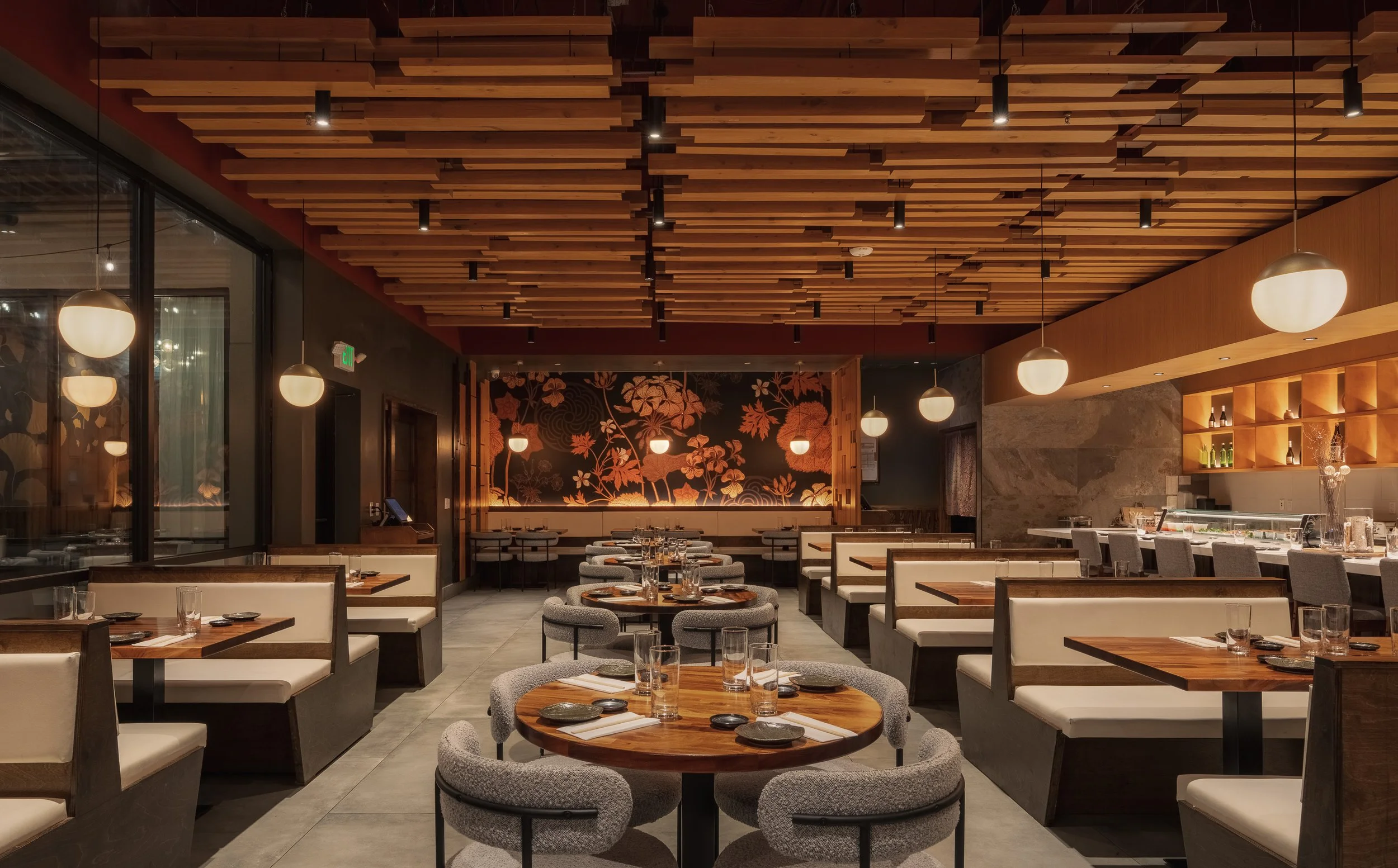 Inside a modern restaurant with wooden ceiling beams, hanging lamps, and neatly arranged tables with chairs, set for dining.