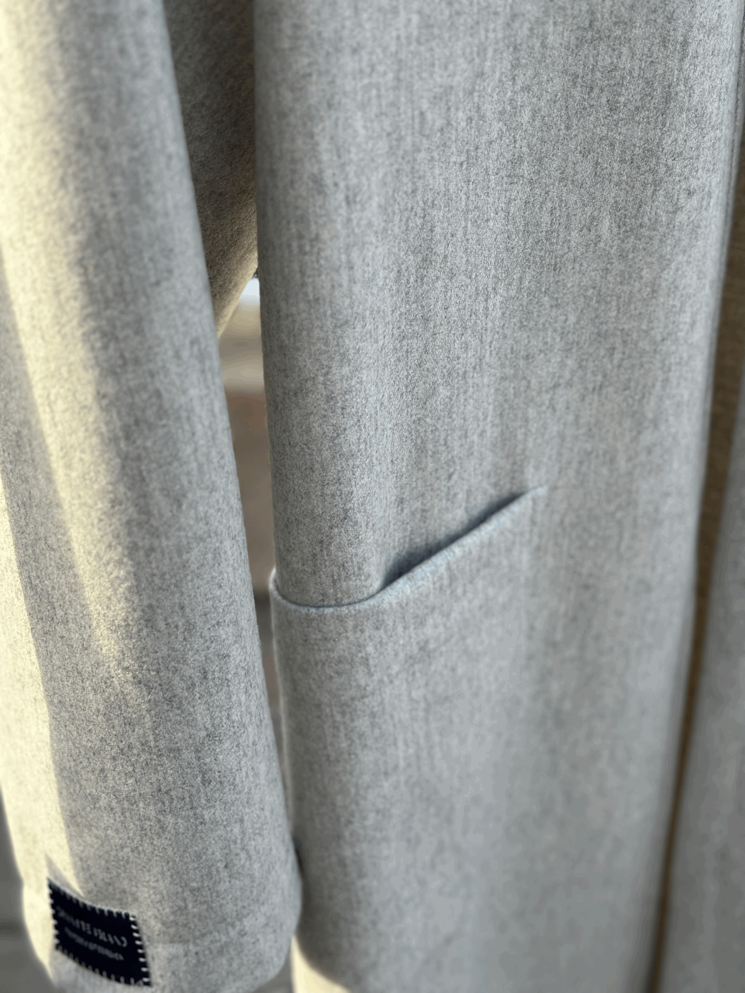 Close-up of the Granite Island Sparkling Ash grey kimono coat, showing the textured fabric, clean stitching and minimalist front pocket.