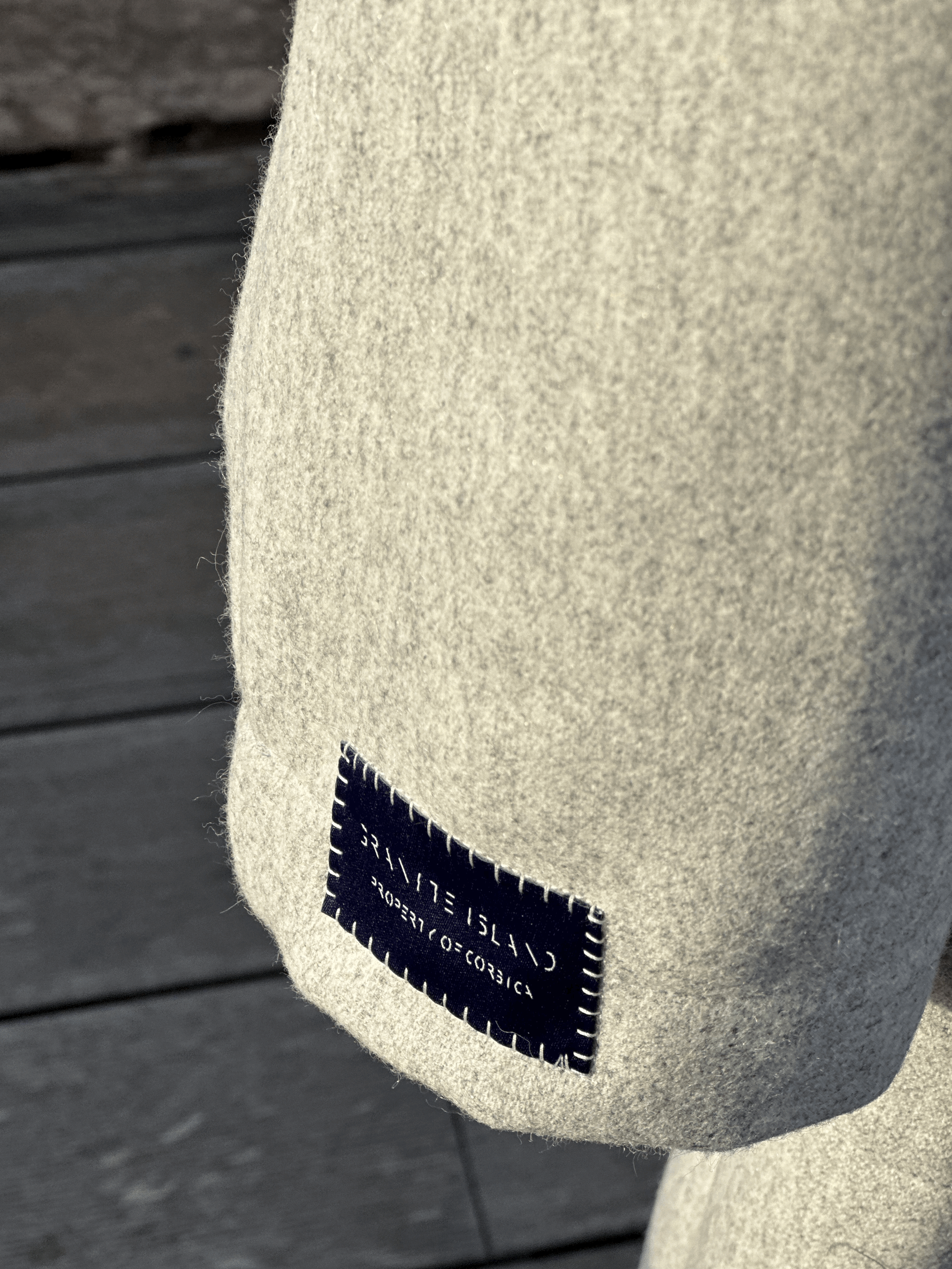 Close-up of the textured grey fabric and Granite Island label on the Sparkling Ash kimono coat, highlighting its refined finish.