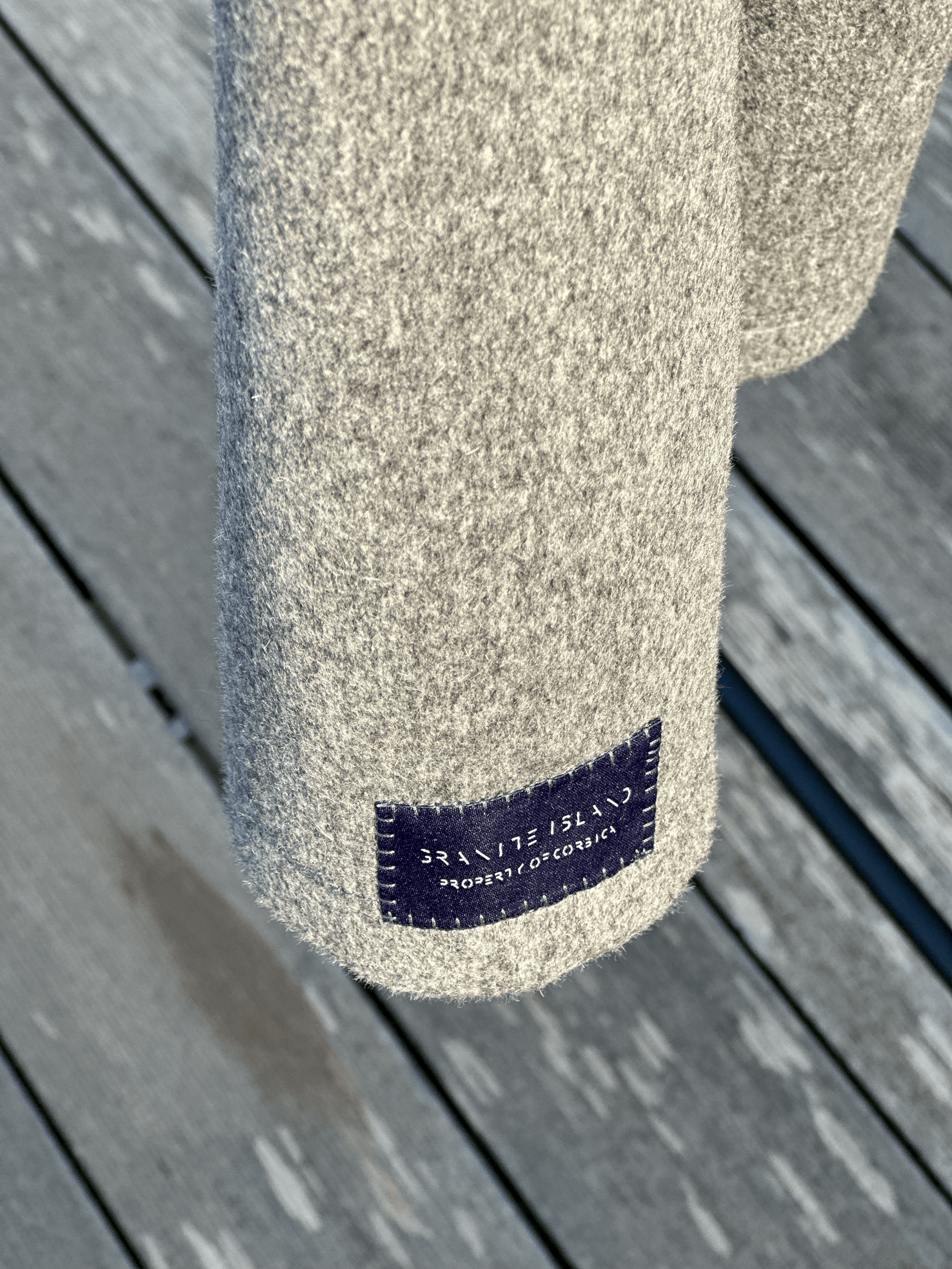 Close-up of the Granite Island Silvery Grey Angora Hoodie, showing its textured grey fabric and dark woven brand label near the hem.