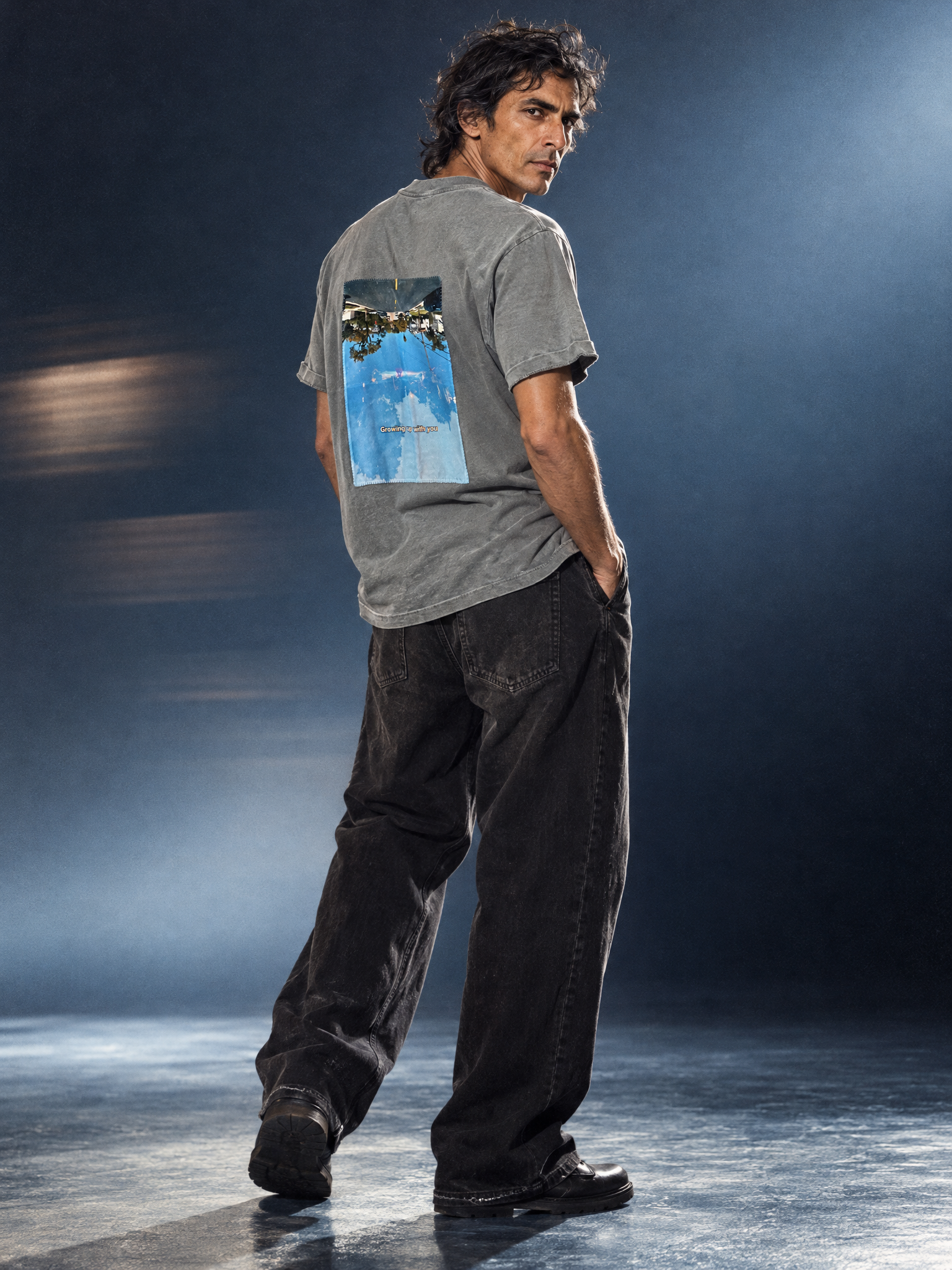 Male model wearing the Granite Island vintage slate grey T-shirt with a blue-toned photographic silk artwork on the back, photographed against a dark blue studio background.