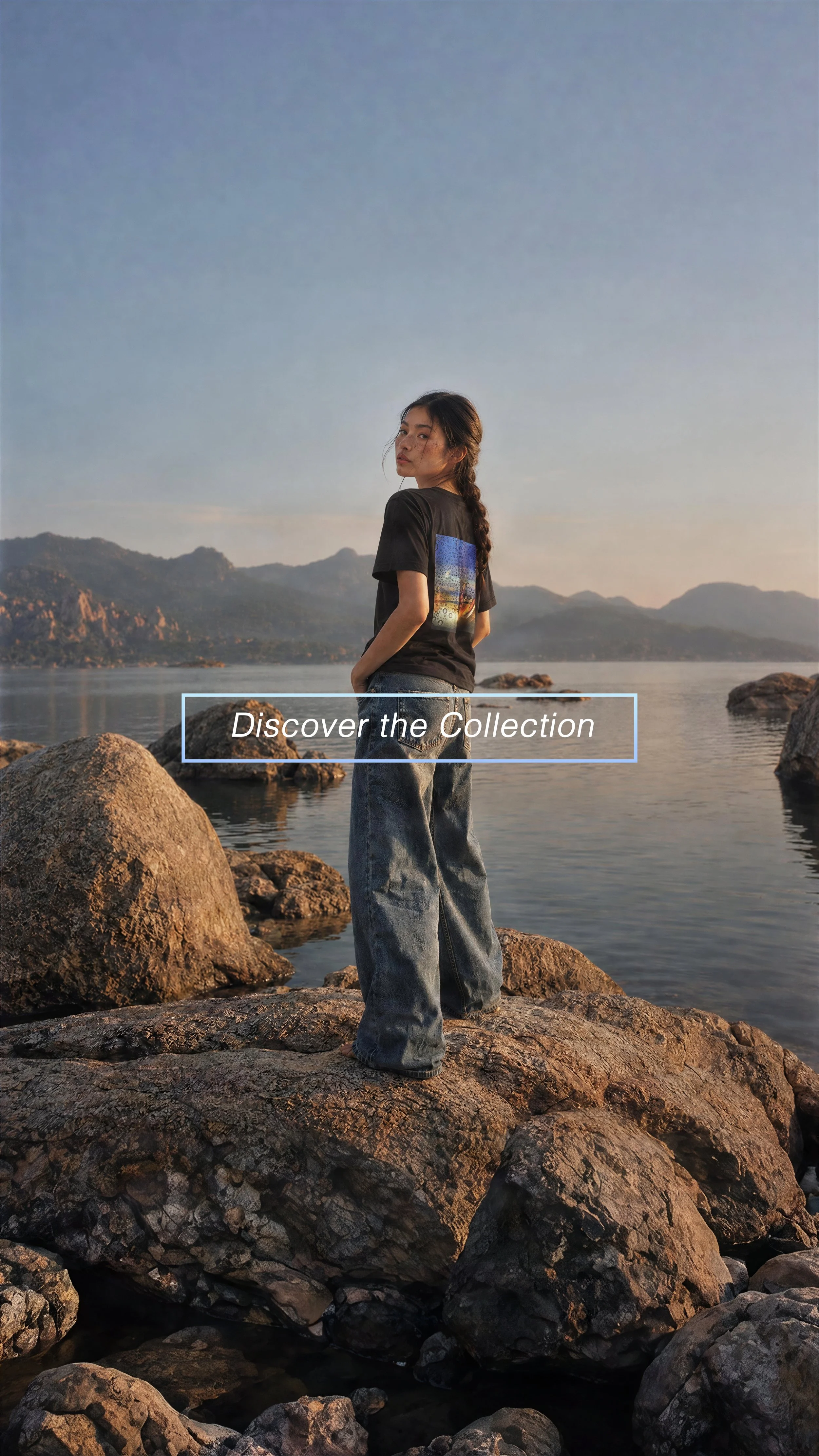 Model wearing a black Granite Island T-shirt featuring fine art photography on silk, standing on the rocky Corsican coastline