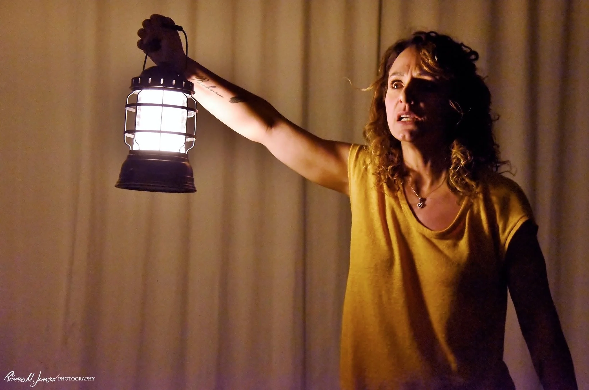 Woman with curly hair holding a lantern in a dimly lit room
