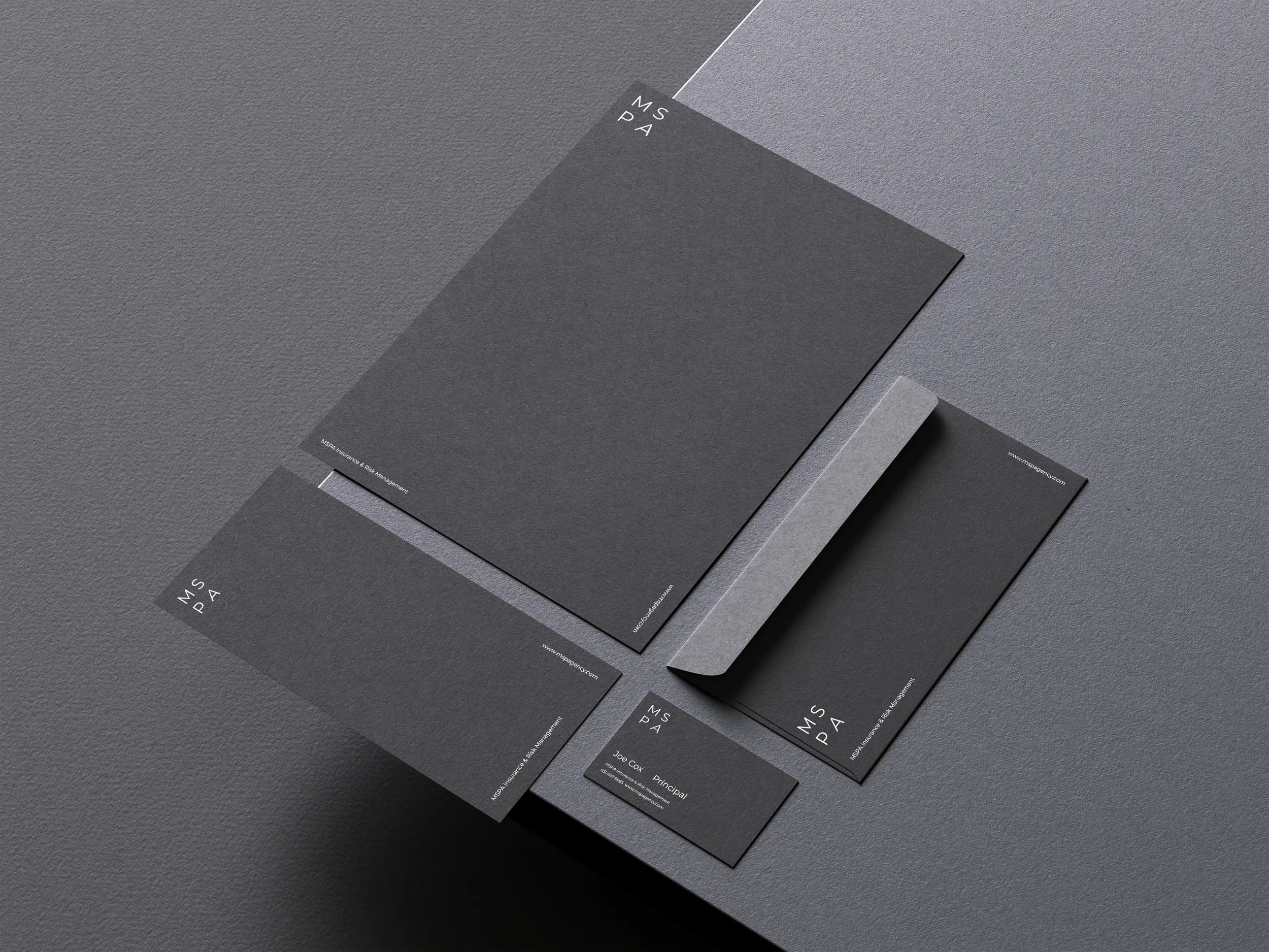 Set of dark gray, minimalist business stationery, including letterhead, envelope, business cards, and folder, arranged on a textured gray surface.