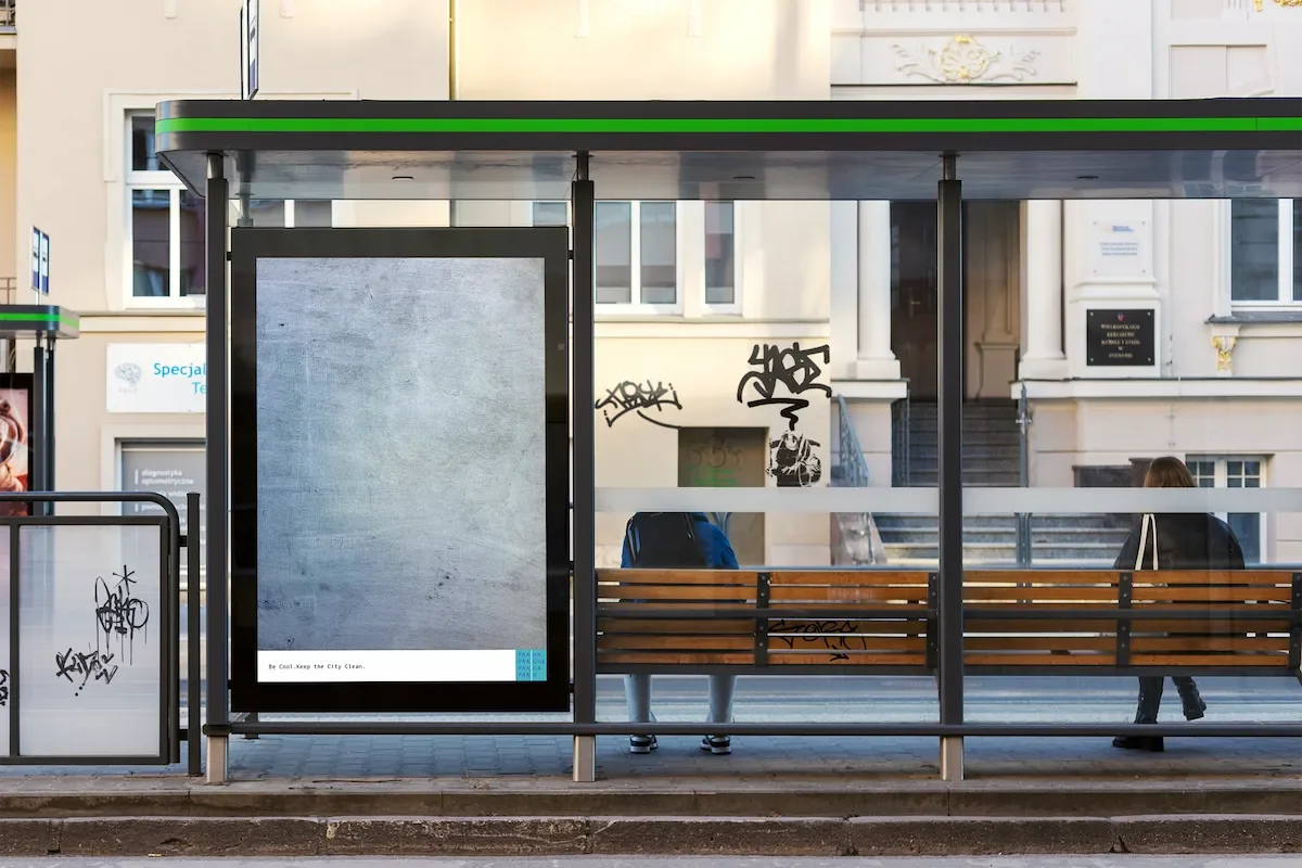 Bus shelter with an empty digital advertising display, graffiti on glass panels, and people sitting and standing outside on a city sidewalk.