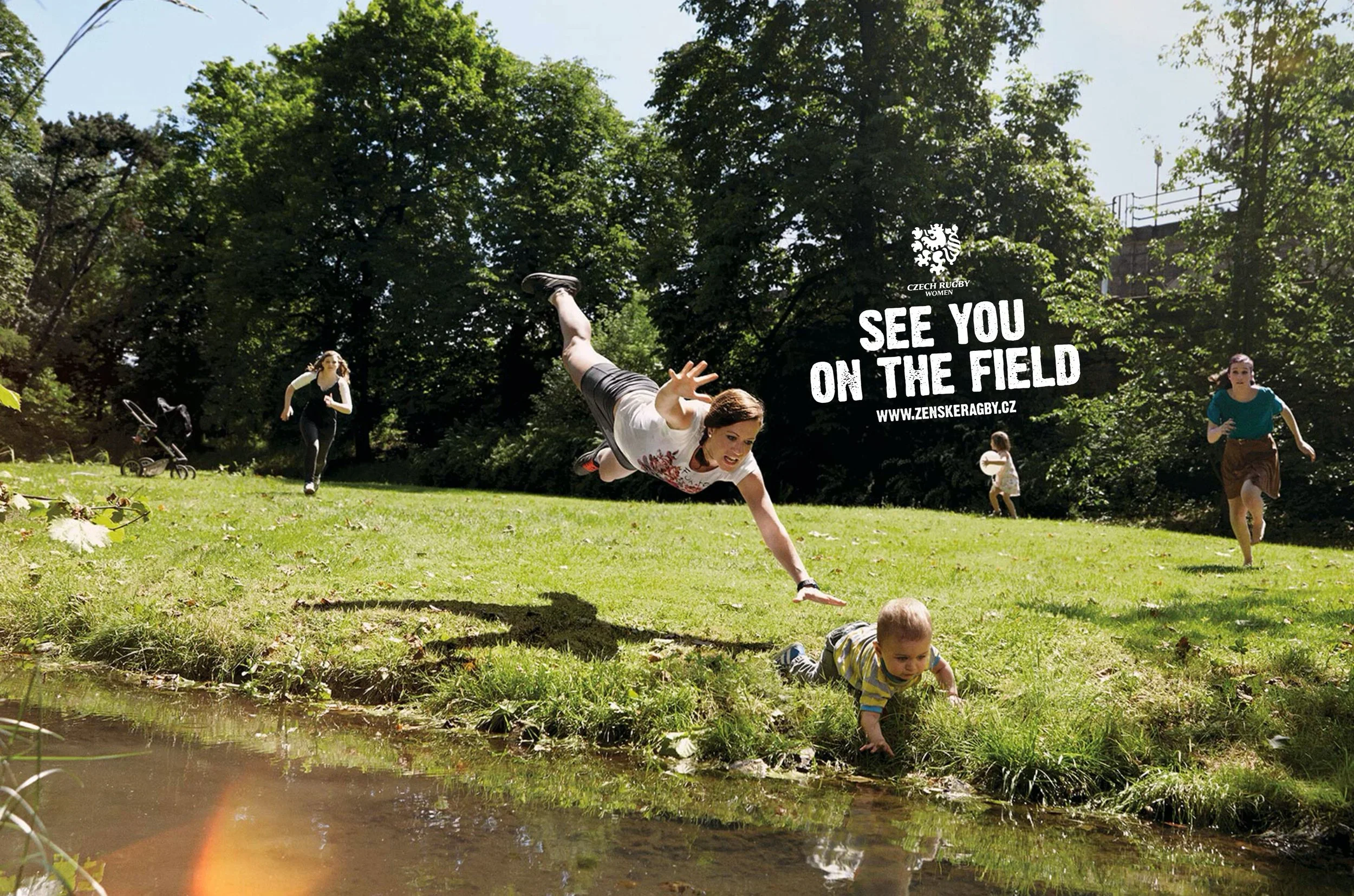 Group of women and children outdoors in a park, with one woman falling or diving towards a crawling baby by a small pond, others walking in the background, and trees surrounding the scene.
