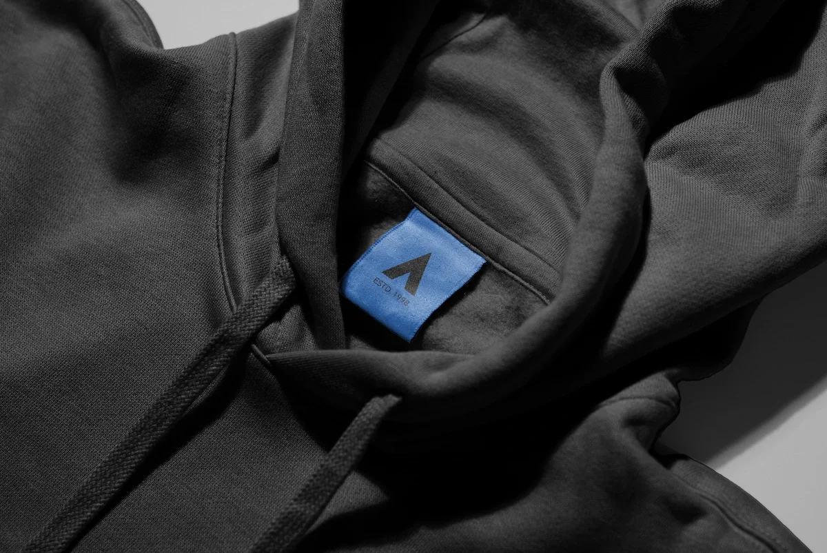 Close-up of a black hoodie with a blue clothing label that has a black logo and text, partially visible.