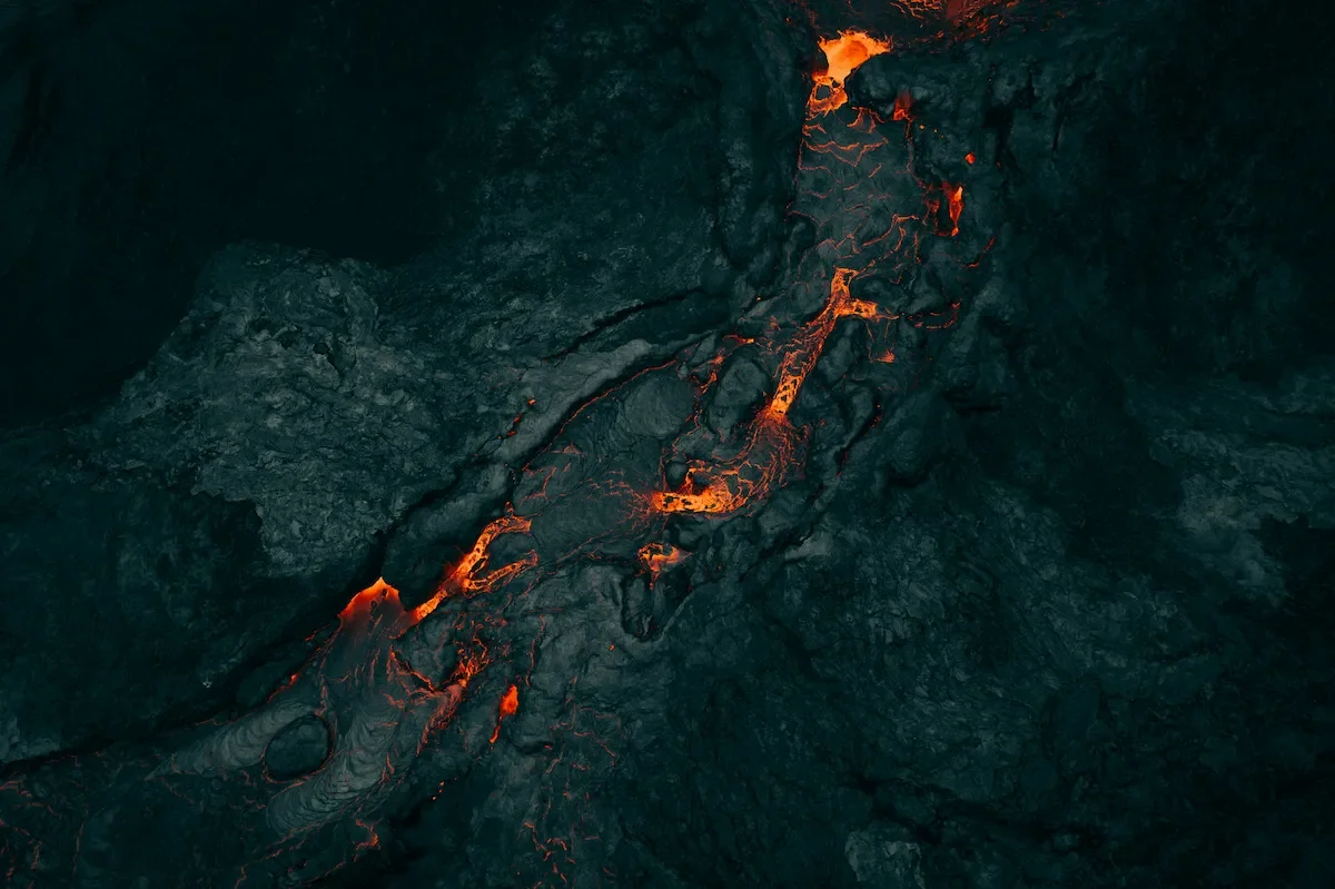 Close-up of flowing lava in a volcanic fissure with glowing orange cracks on dark volcanic rock.
