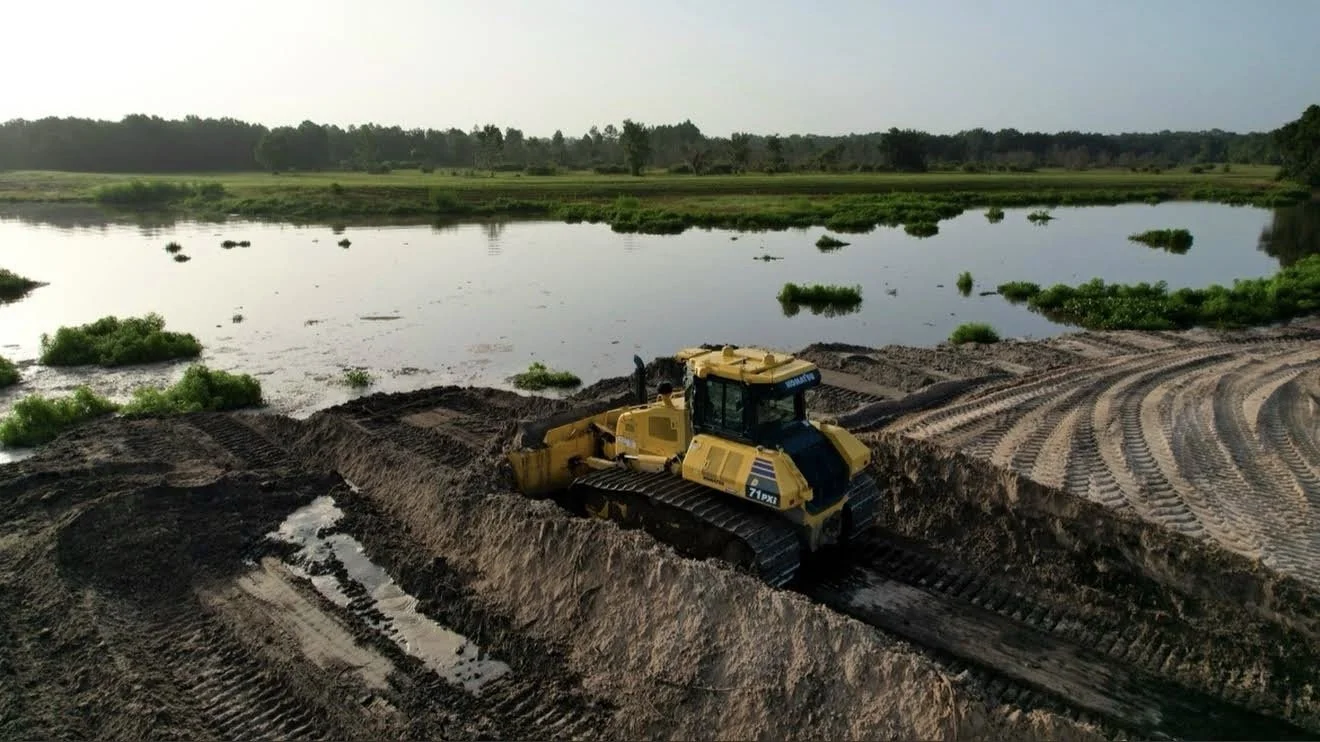 Komatsu bulldozer pushing dirt at the edge of a pond on a Knepp Construction site preparation project