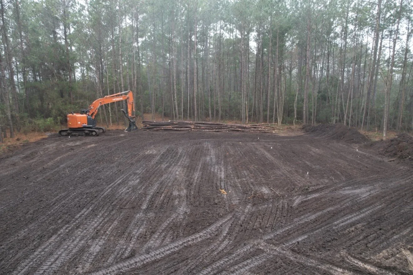 Hitachi excavator on freshly cleared land with stacked timber on a Knepp Construction land clearing project