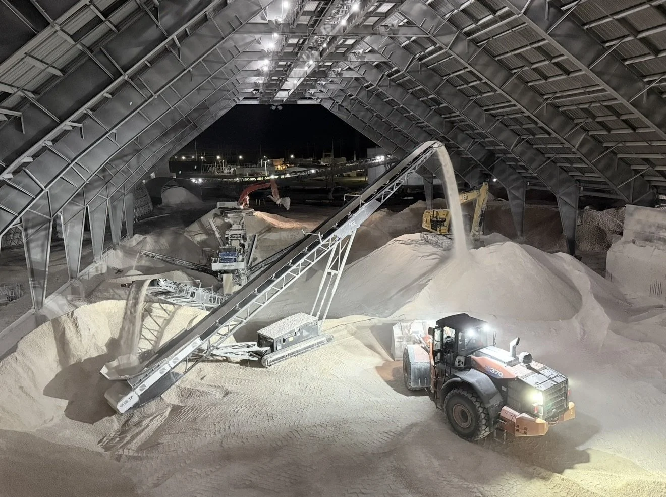 Nighttime crushing operation inside a covered storage facility with conveyors stockpiling crushed aggregate
