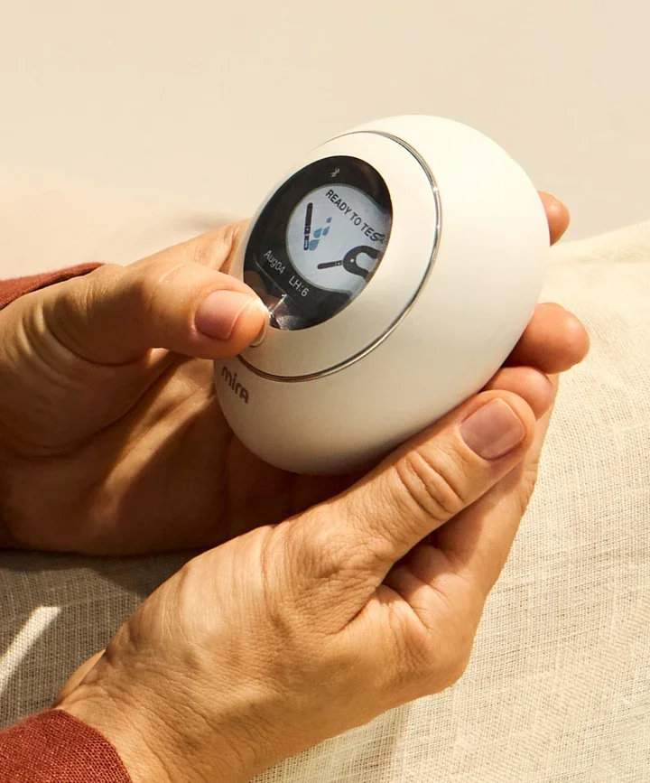 A person holding a white digital thermometer with a circular display, showing a temperature of 99.4°F and a message 'Ready to Test'.