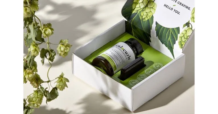 Open white box containing a dark bottle labeled "allcub" and a small black object, with green leaf-patterned interior and greeting note.