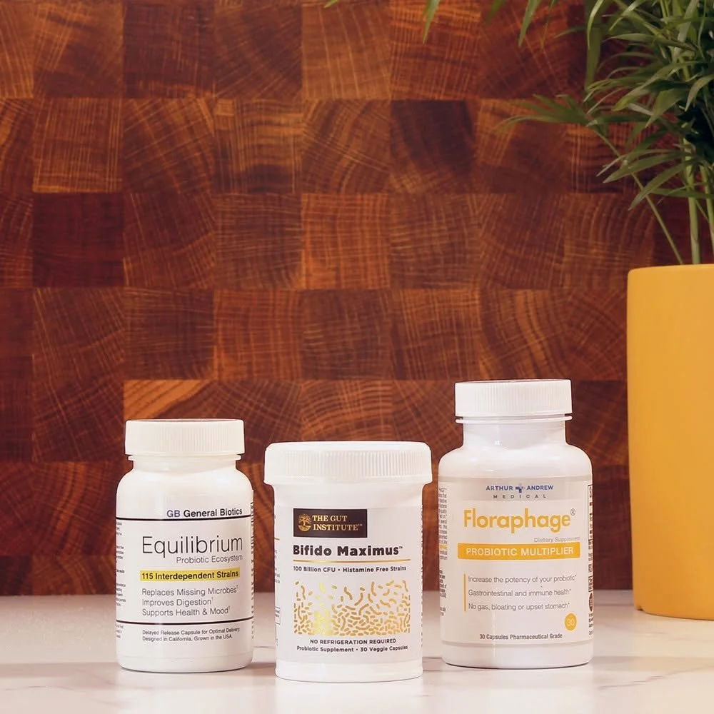 Three bottles of dietary supplements on a white surface against a wooden wall, with a yellow pot and green plant on the right side.