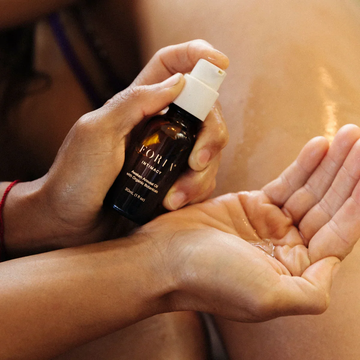 Person spraying intimate oil from a small brown bottle onto palm.