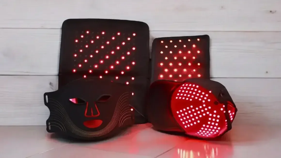 Two LED masks and two LED glasses with red light patterns resting on a white wooden surface.