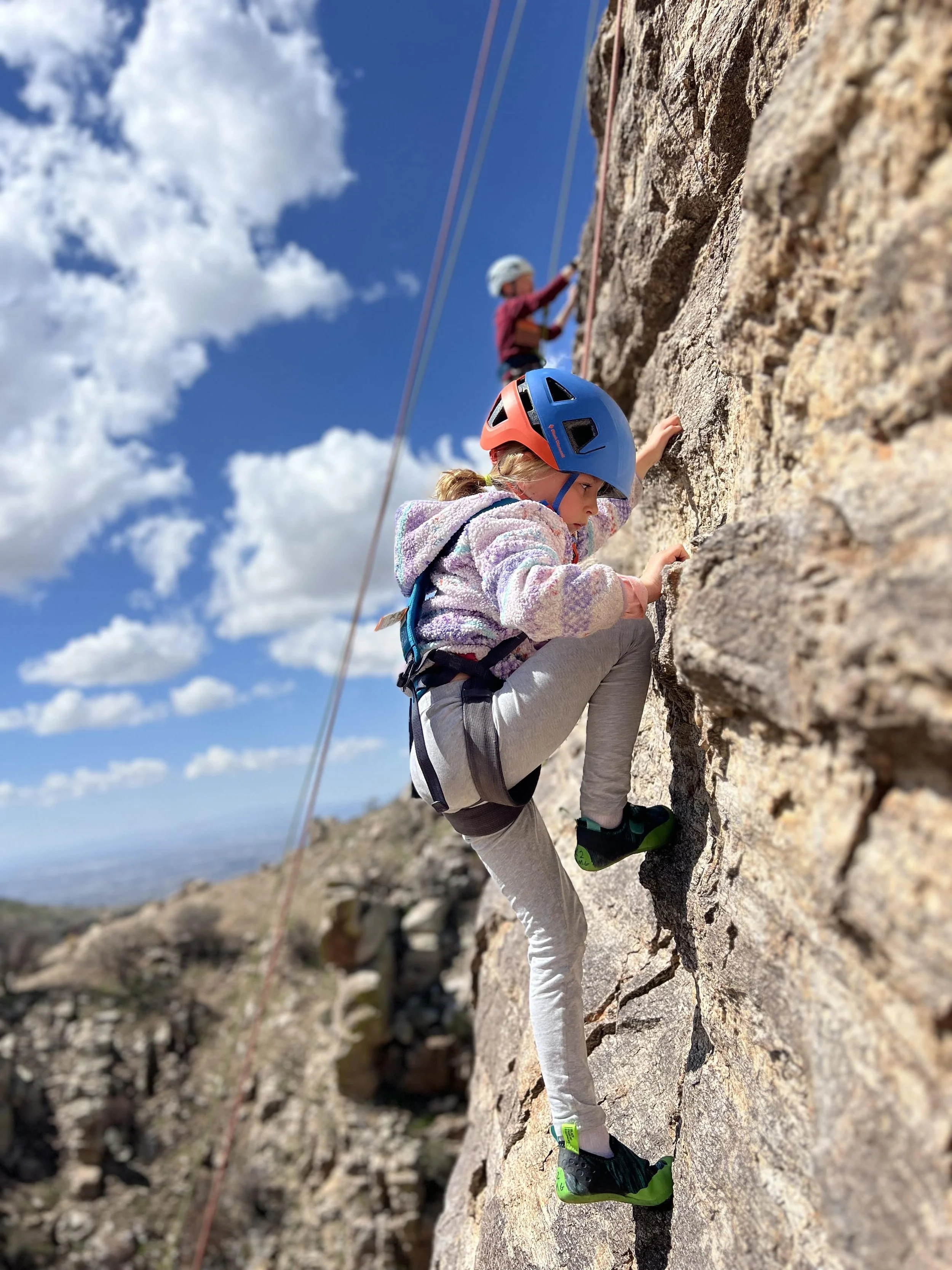 Young girl rock climbing outdoors on Mount Lemmon with another climber above.