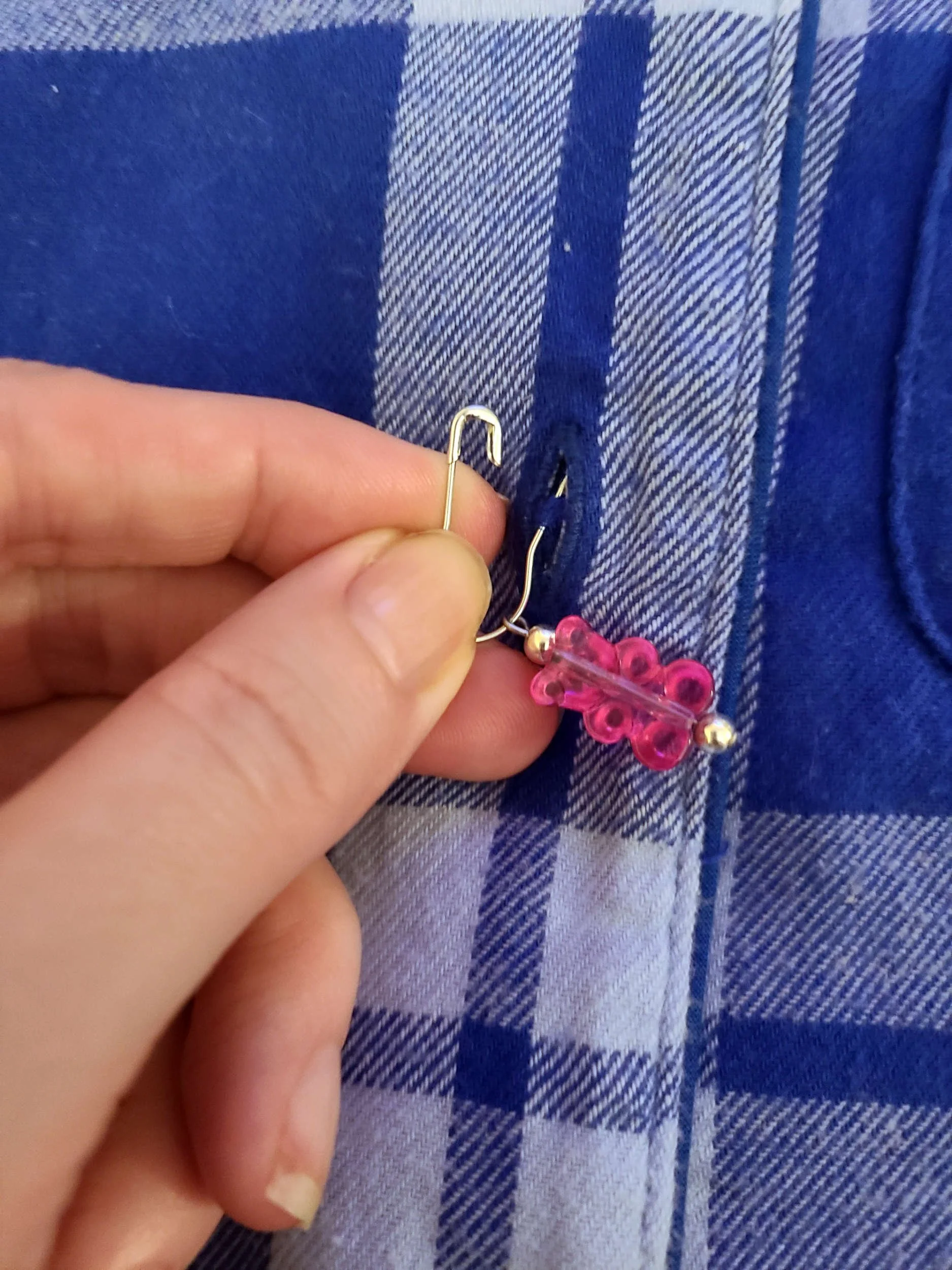 Photo of an open safety pin going through a buttonhole on a flannel shirt and picking up fabric on the next layer.