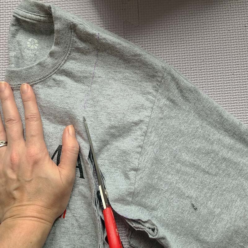 Photo of scissors cutting along the armhole of a gray T-shirt.