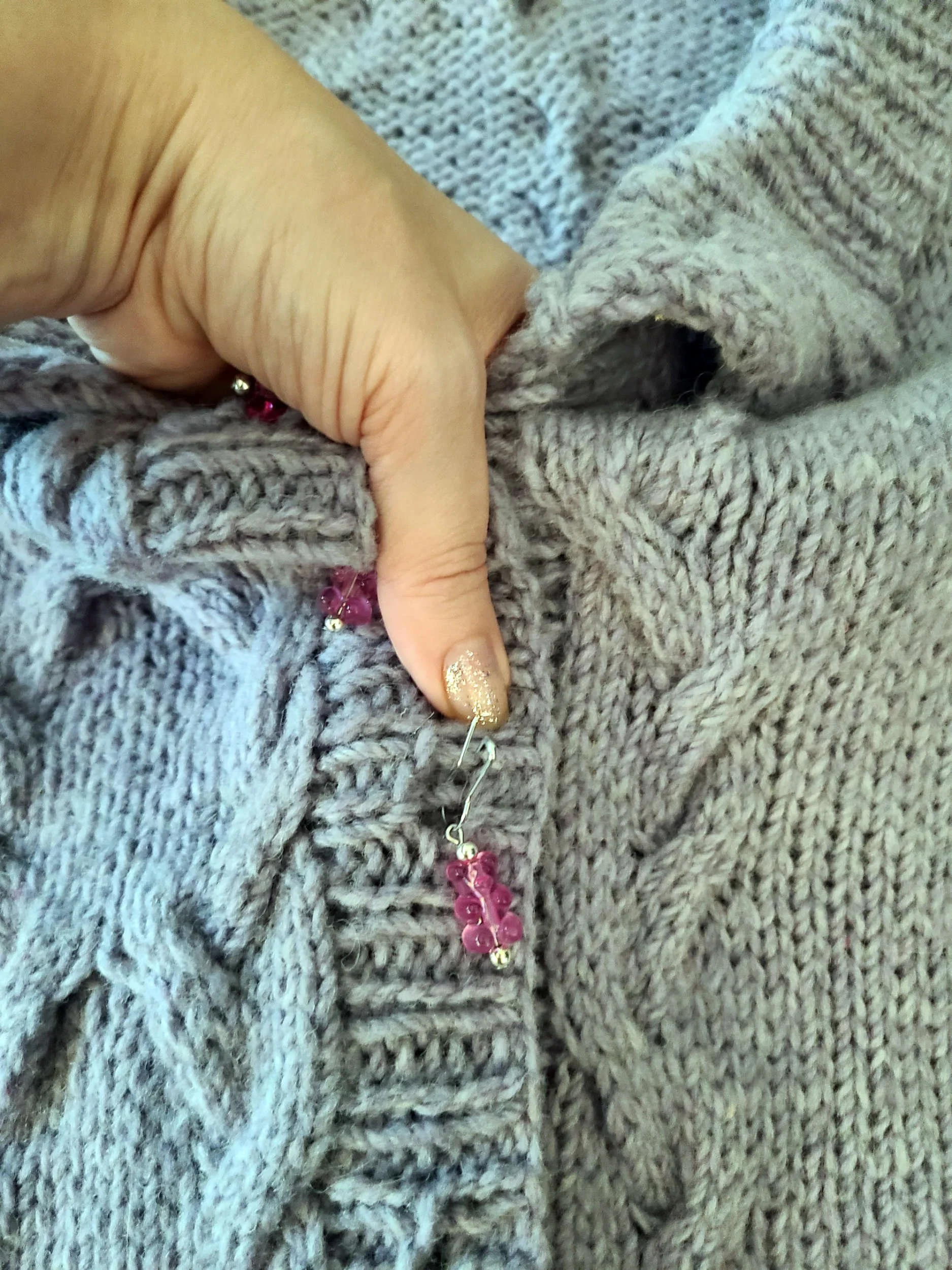 Photo of a human hand bracing the top of a knit cardigan button band in order to better reach a buttonhole in the middle of the garment.