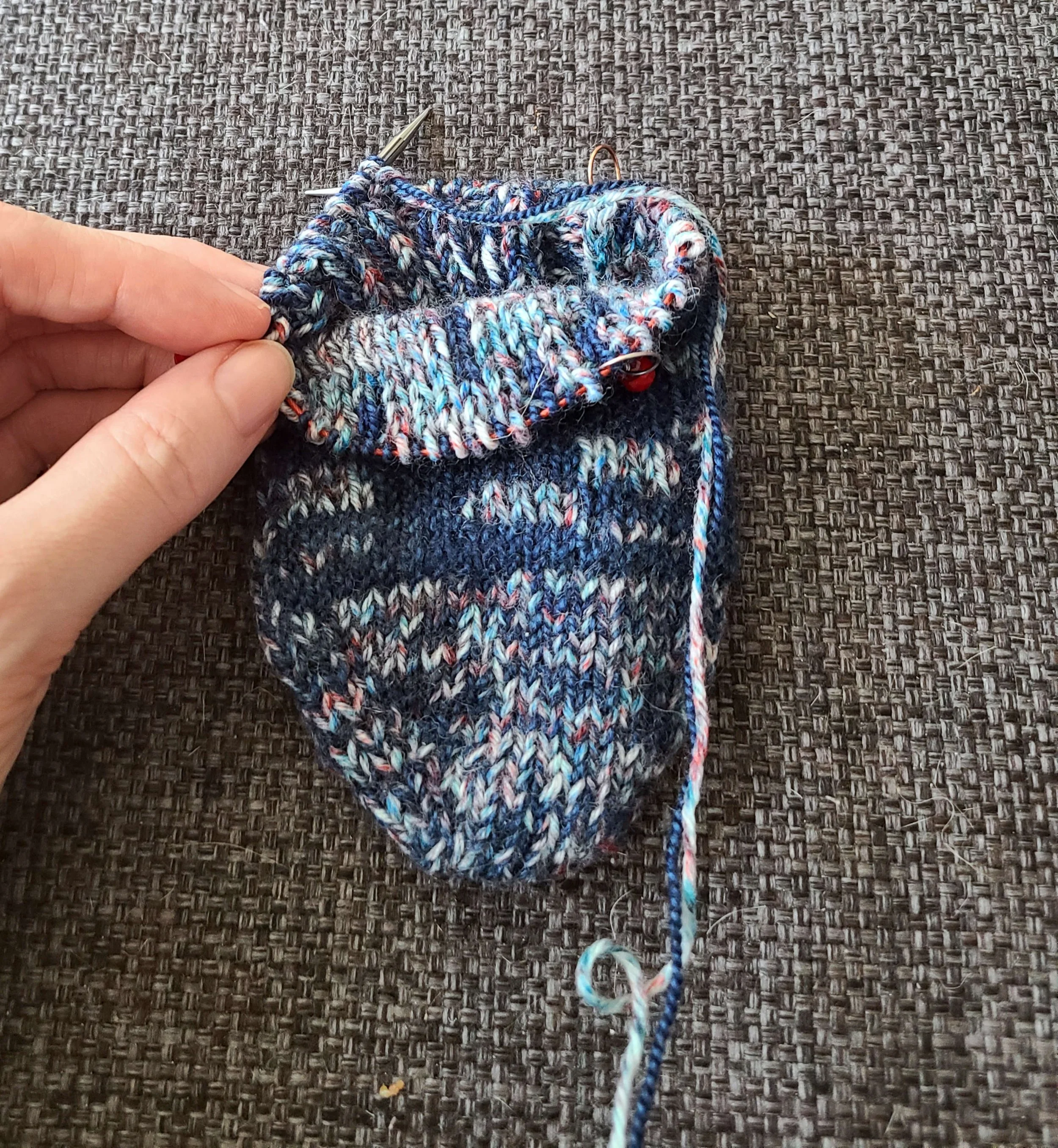 Photo of a handknit sock on the needles. The top of the sock is folded down to show that there are "right side" knit stitches visible both on the inside and outside of the sock.