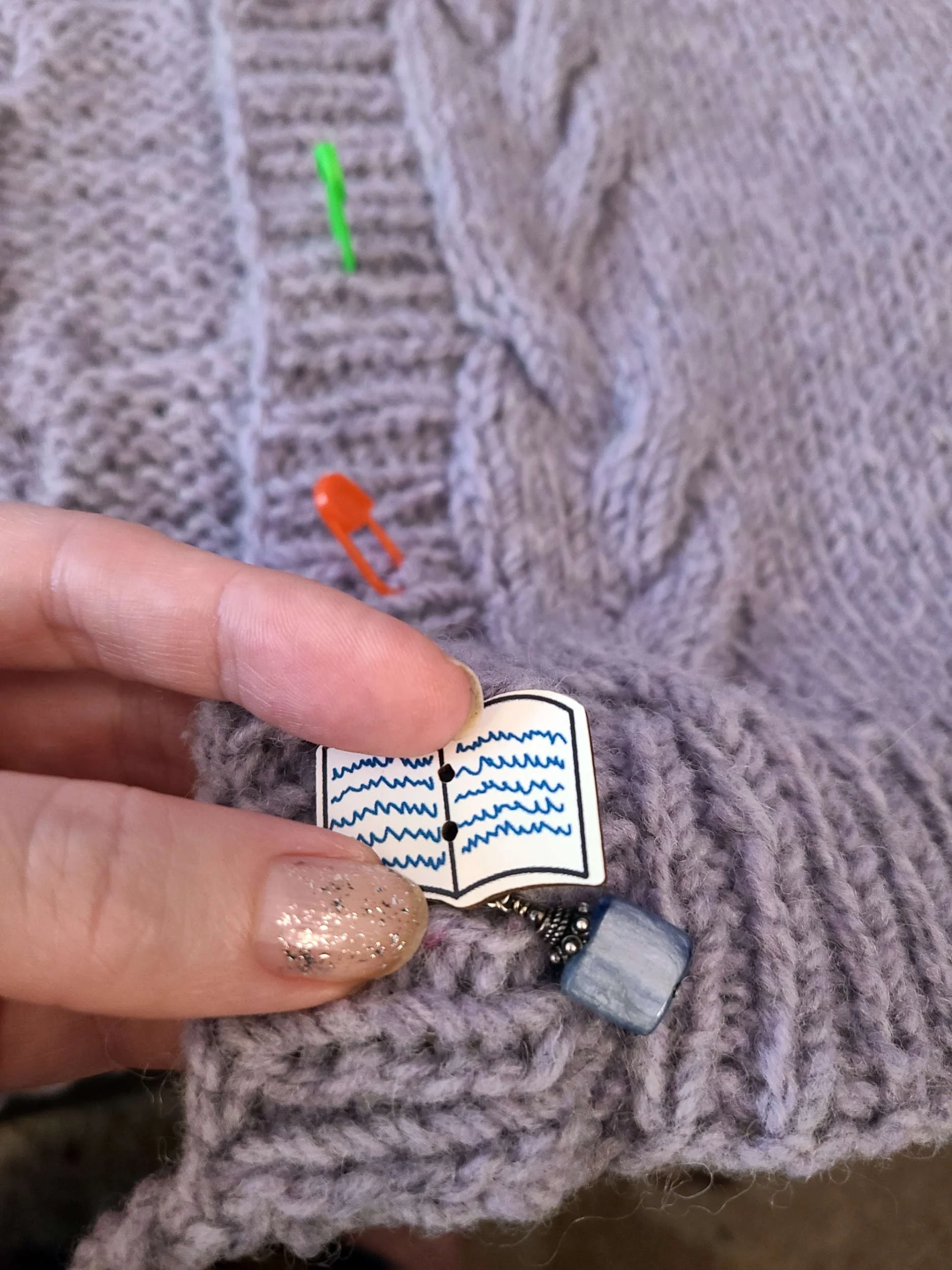 Photo of an unsewn button being positioned on a knit cardigan directly over a stitch marker.
